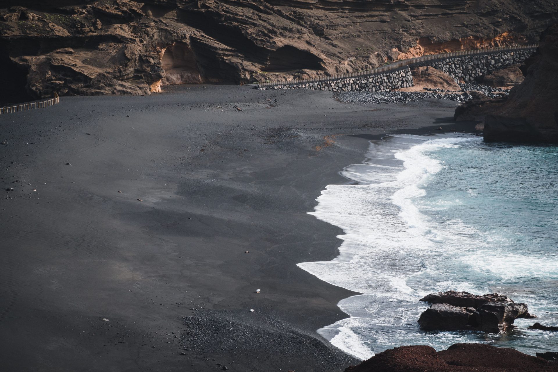 A black sand beach and turquoise surf below brown volcanic cliffs on Lanzarote in the Canary Islands
