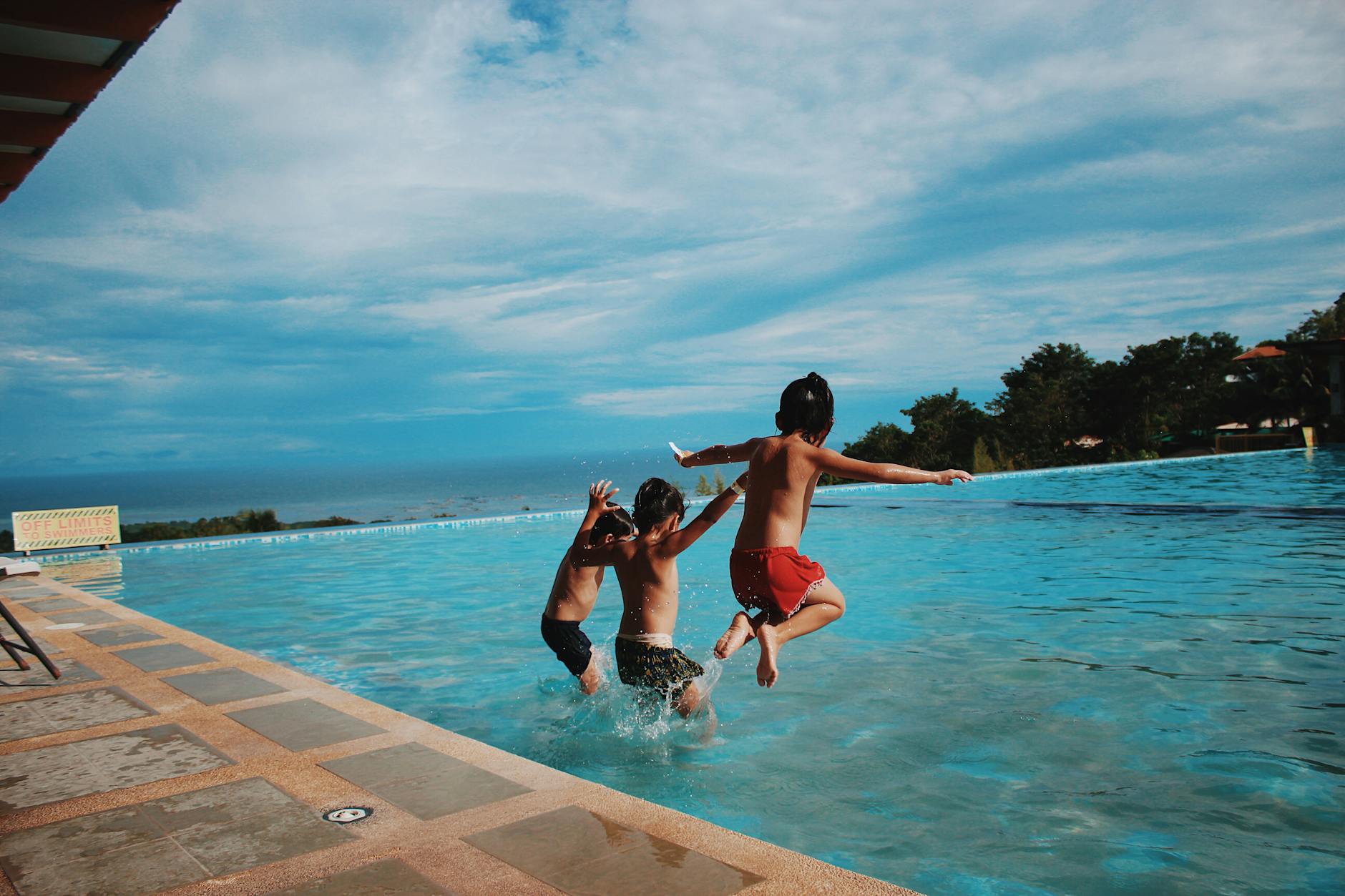 Kids jumping into a resort swimming pool on a sunny vacation day