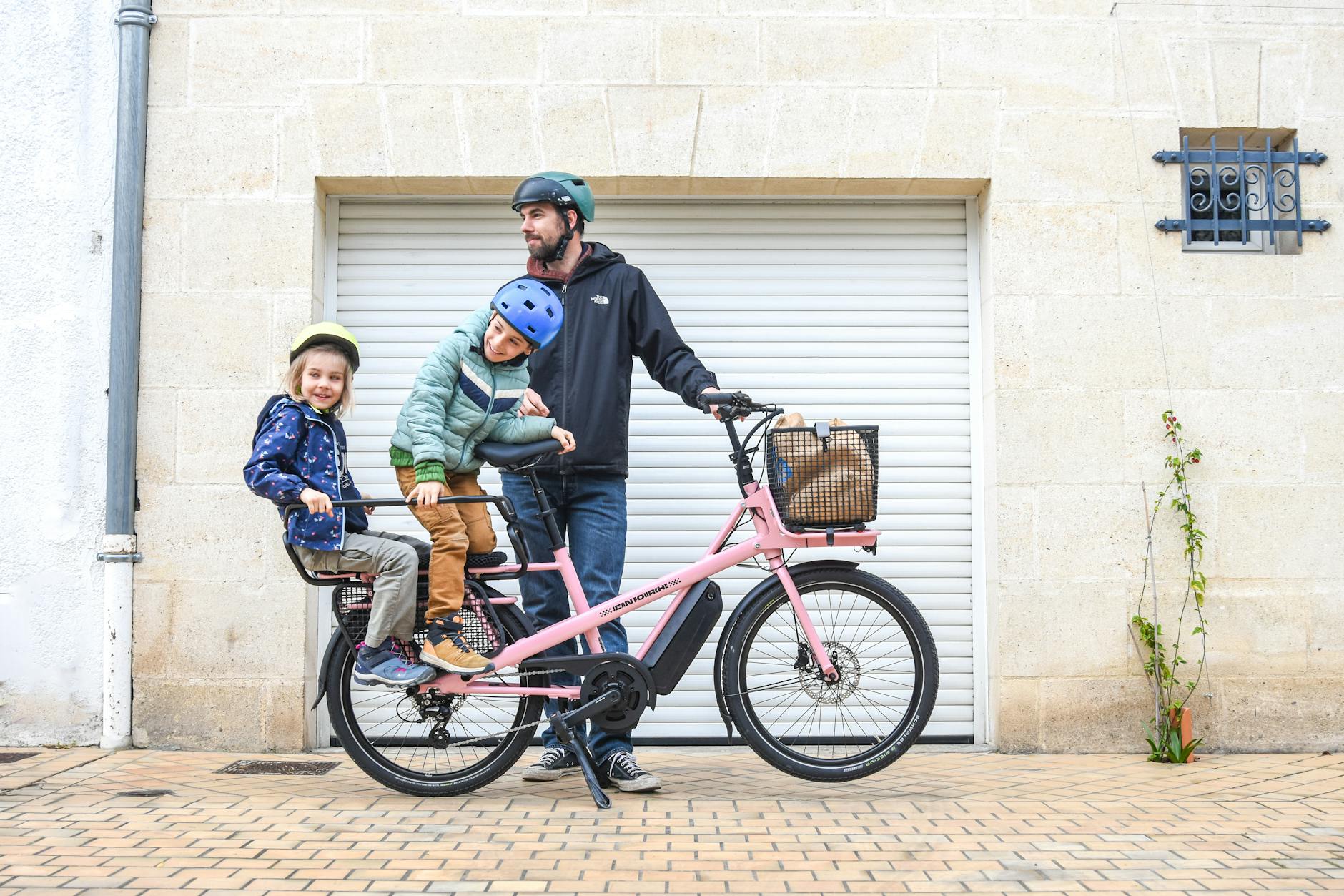 Parent and two helmeted kids on a family cargo bike &mdash; typical Amsterdam and Copenhagen school-run scene.