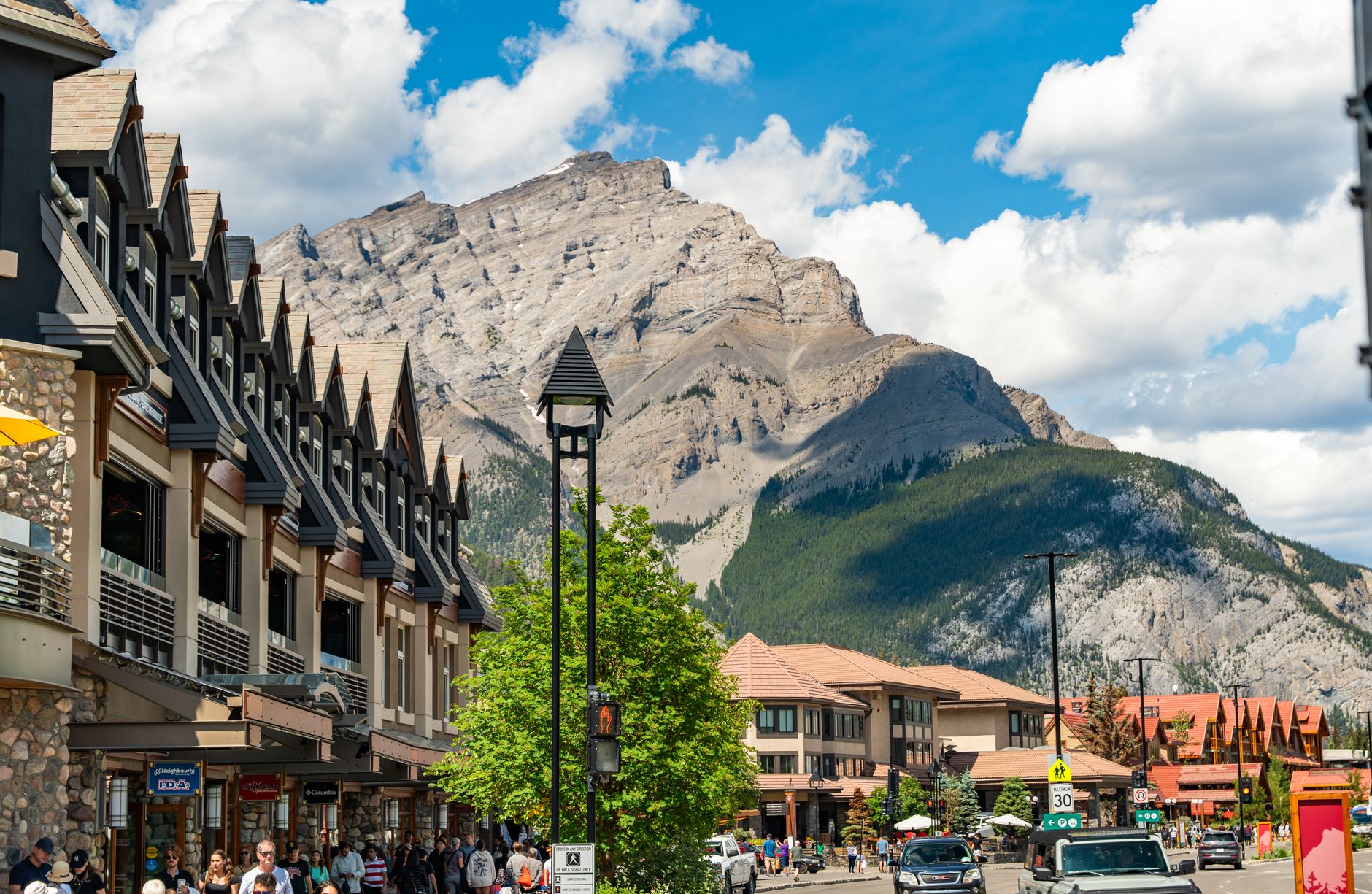 A Banff town street with the Canadian Rockies rising behind on a summer day &mdash; the walkable townsite base for a Bow Valley family stay