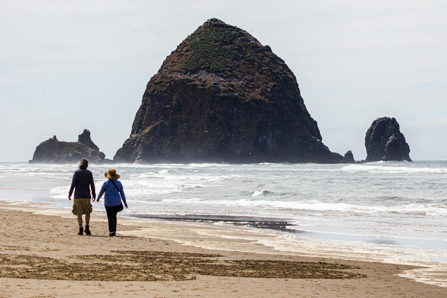 Cannon Beach, Oregon shoreline with two people walking and Haystack Rock rising from the water