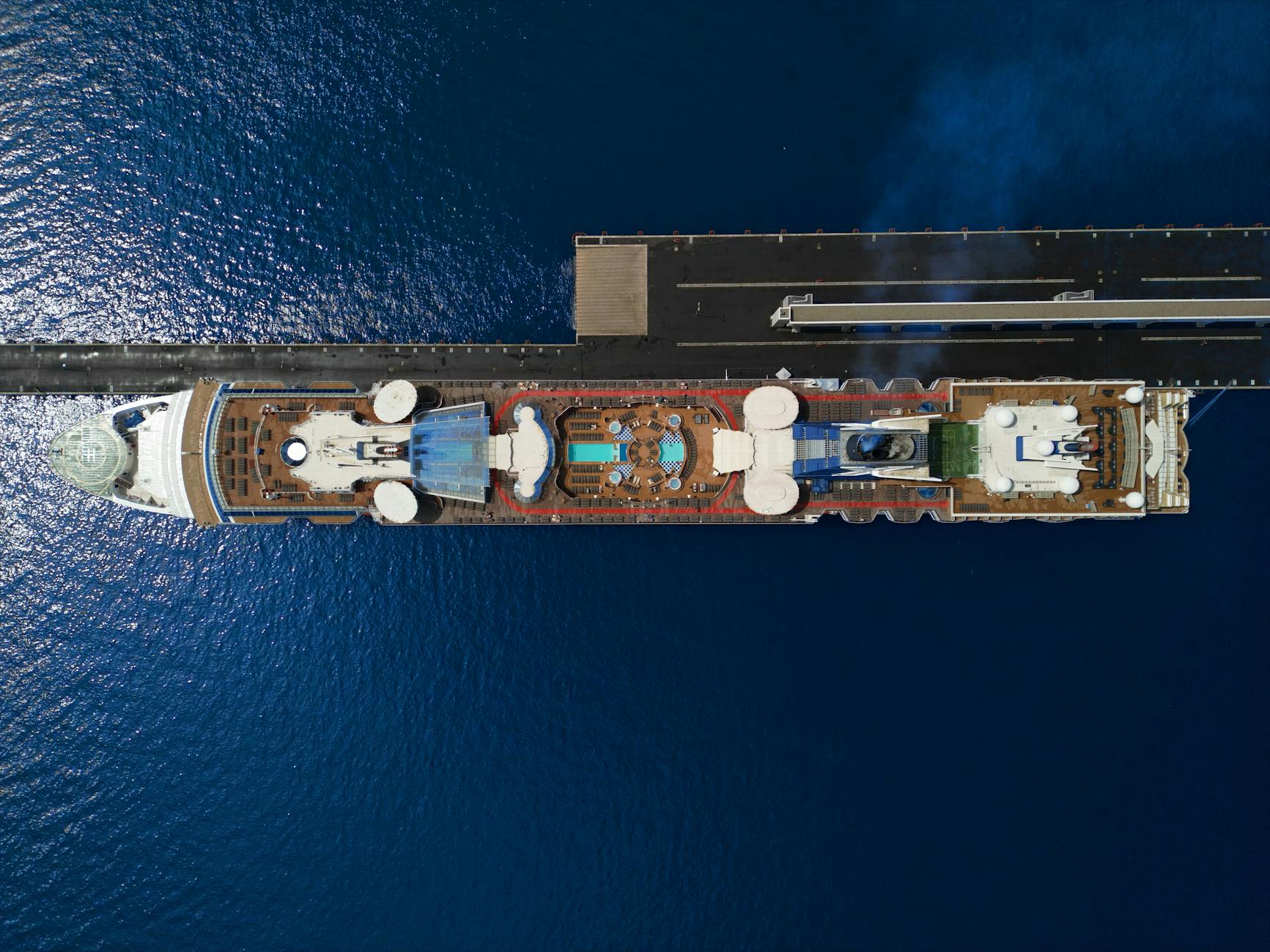 Top-down view of a large cruise ship with pool deck docked at a port