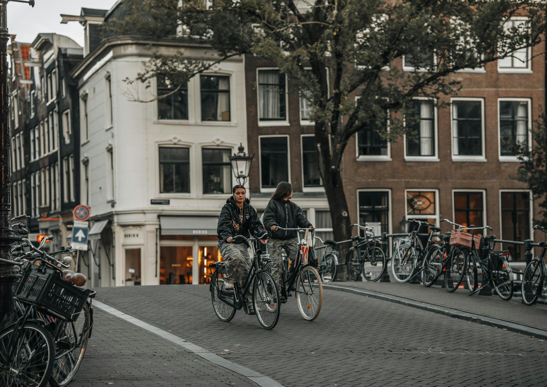 Cyclists crossing a historic canal bridge in Amsterdam lined with parked bicycles