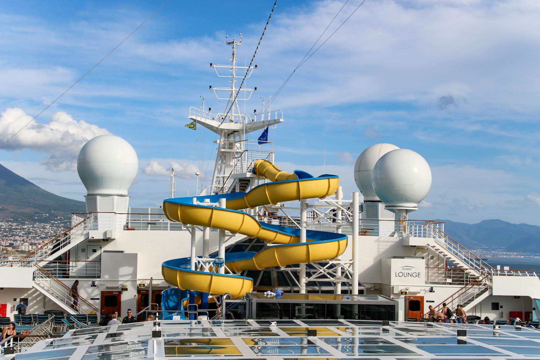 Cruise ship deck featuring a yellow waterslide with ocean views in the background