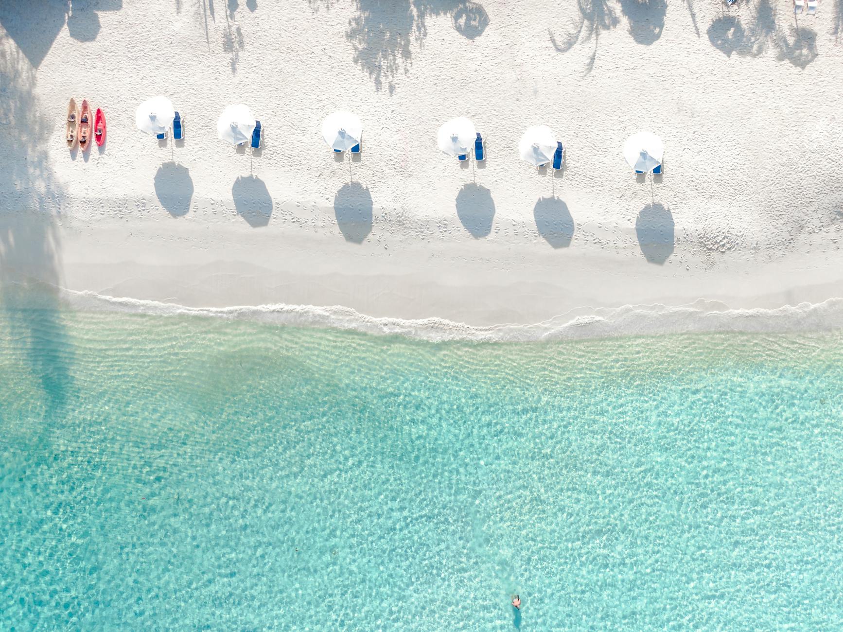 Beach umbrellas and turquoise water at a Caribbean resort beach from above