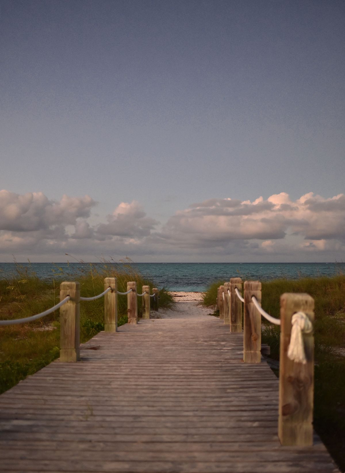 Wooden boardwalk with rope rails leading to a quiet beach in Turks and Caicos at dusk