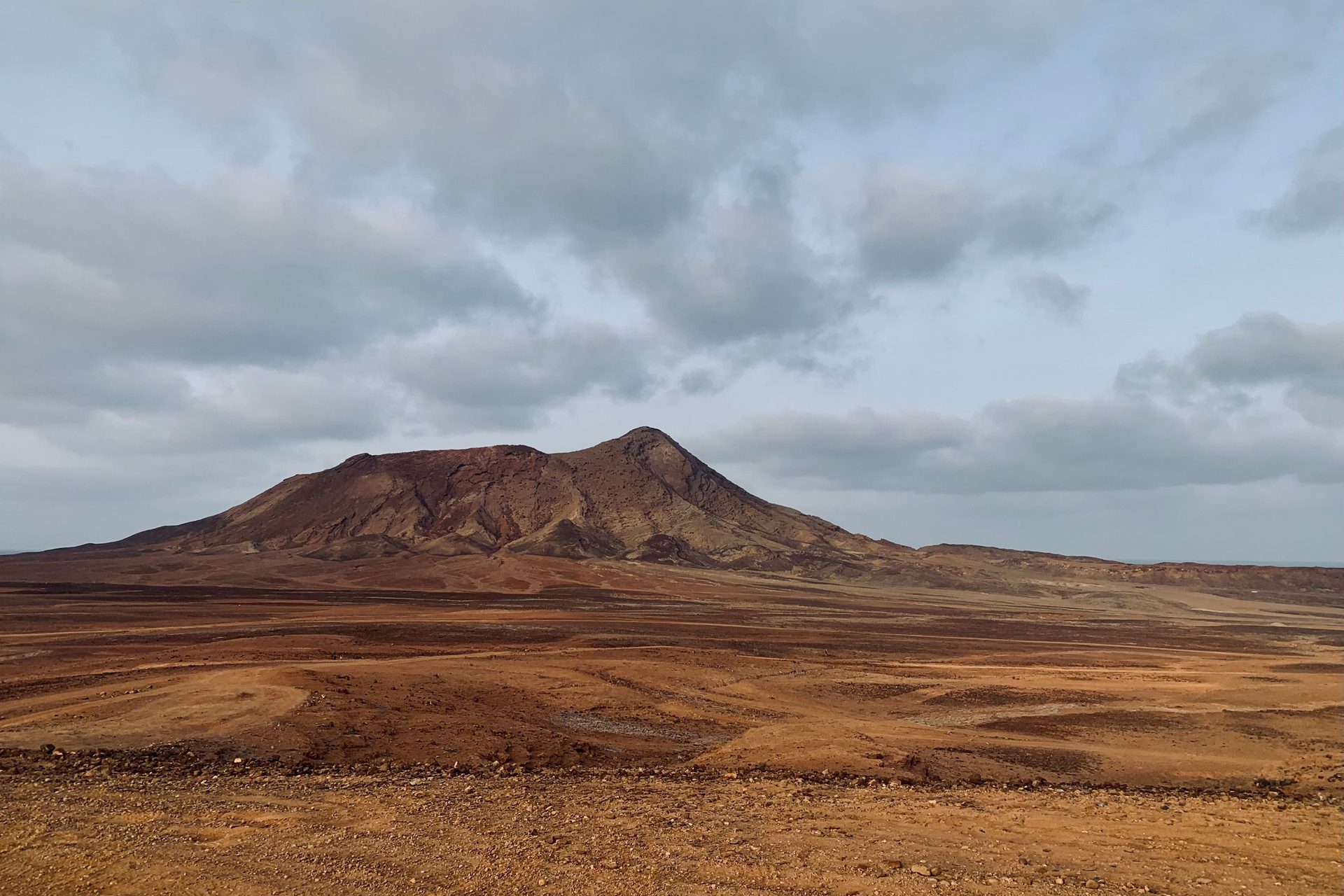 The dry interior of Sal, Cape Verde: a brown volcanic hill above flat, stony ground under grey cloud