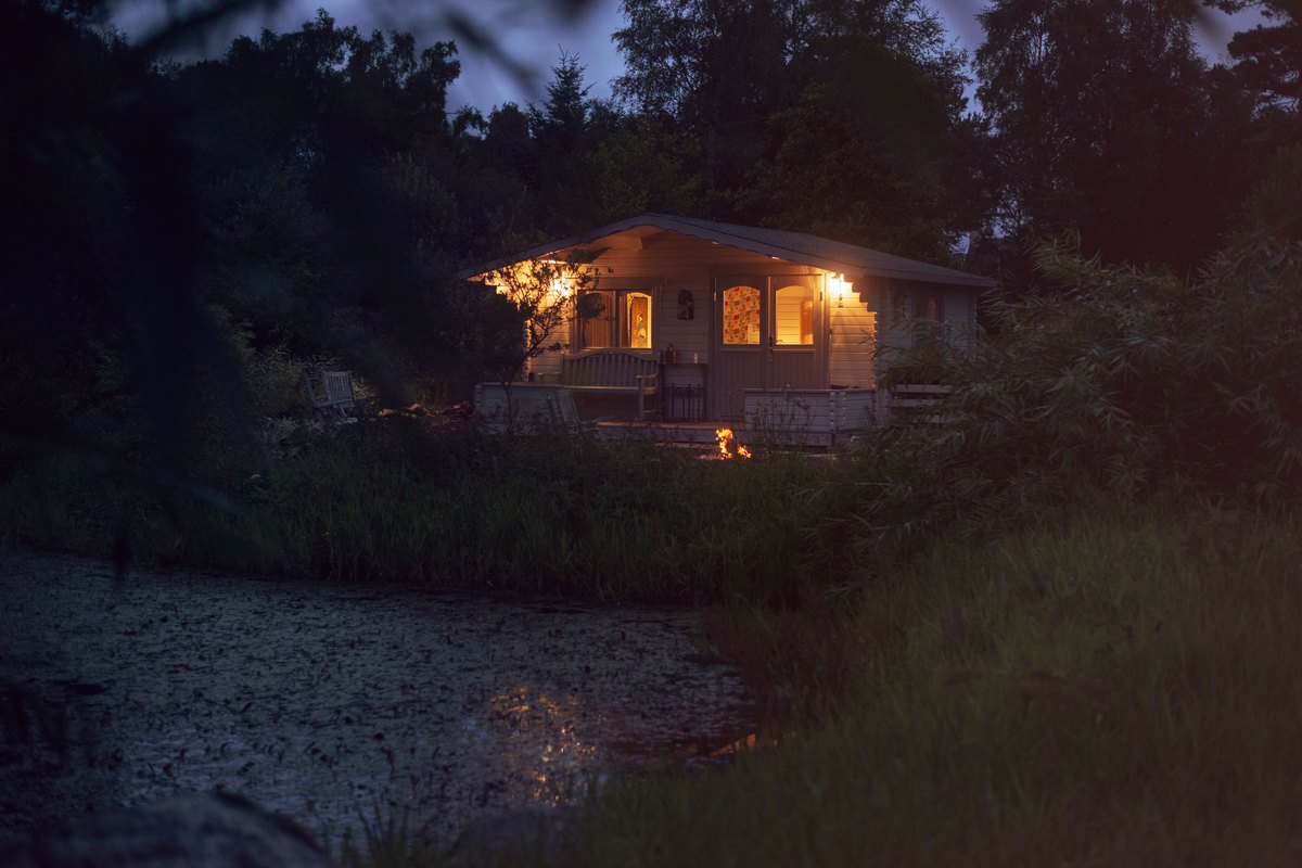 Lit wooden cabin by a pond at twilight, the evening rhythm of a forest village break
