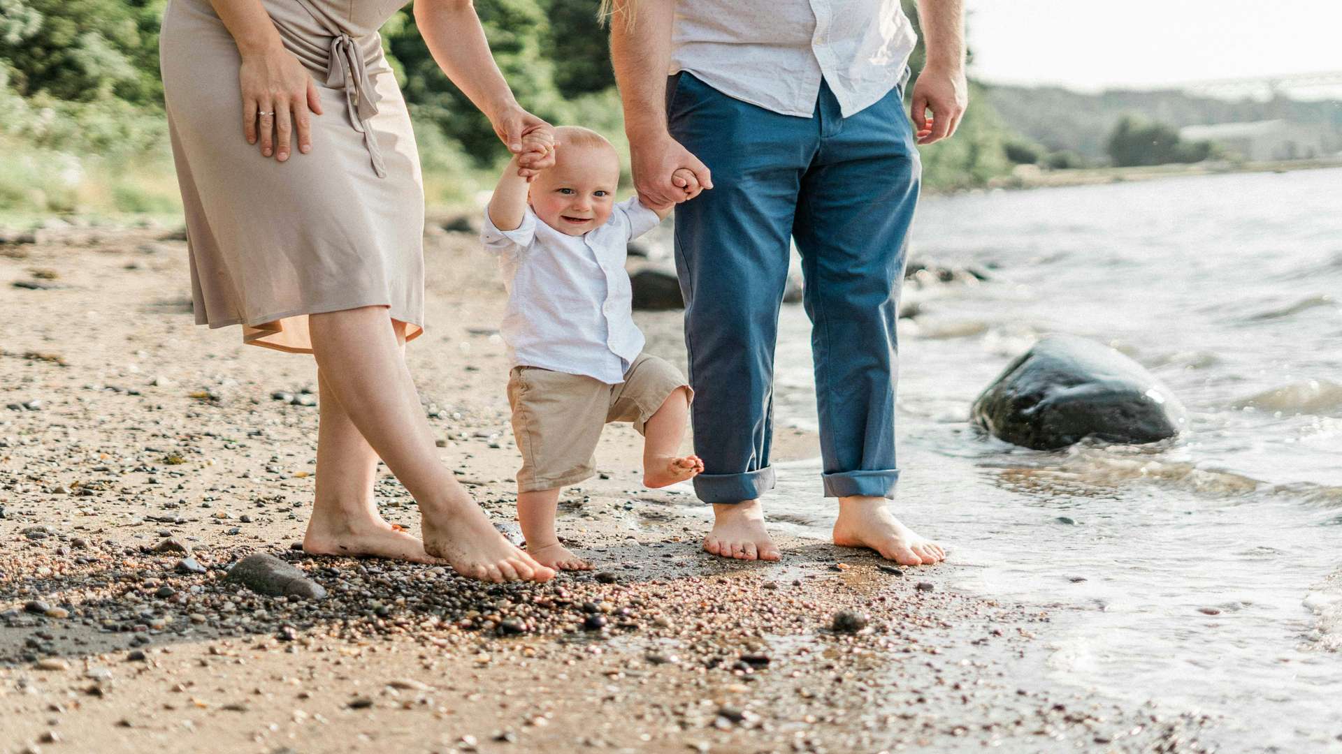 Parents holding a toddler's hands at the water's edge on a cheap family holiday beach