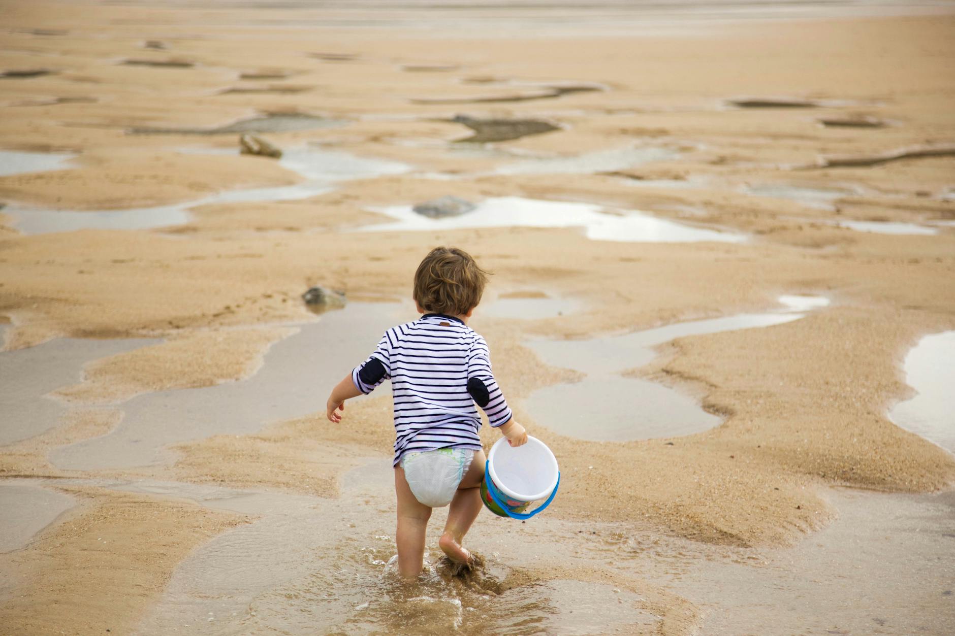 Young child carrying a bucket walking along a sandy beach on a sunny holiday