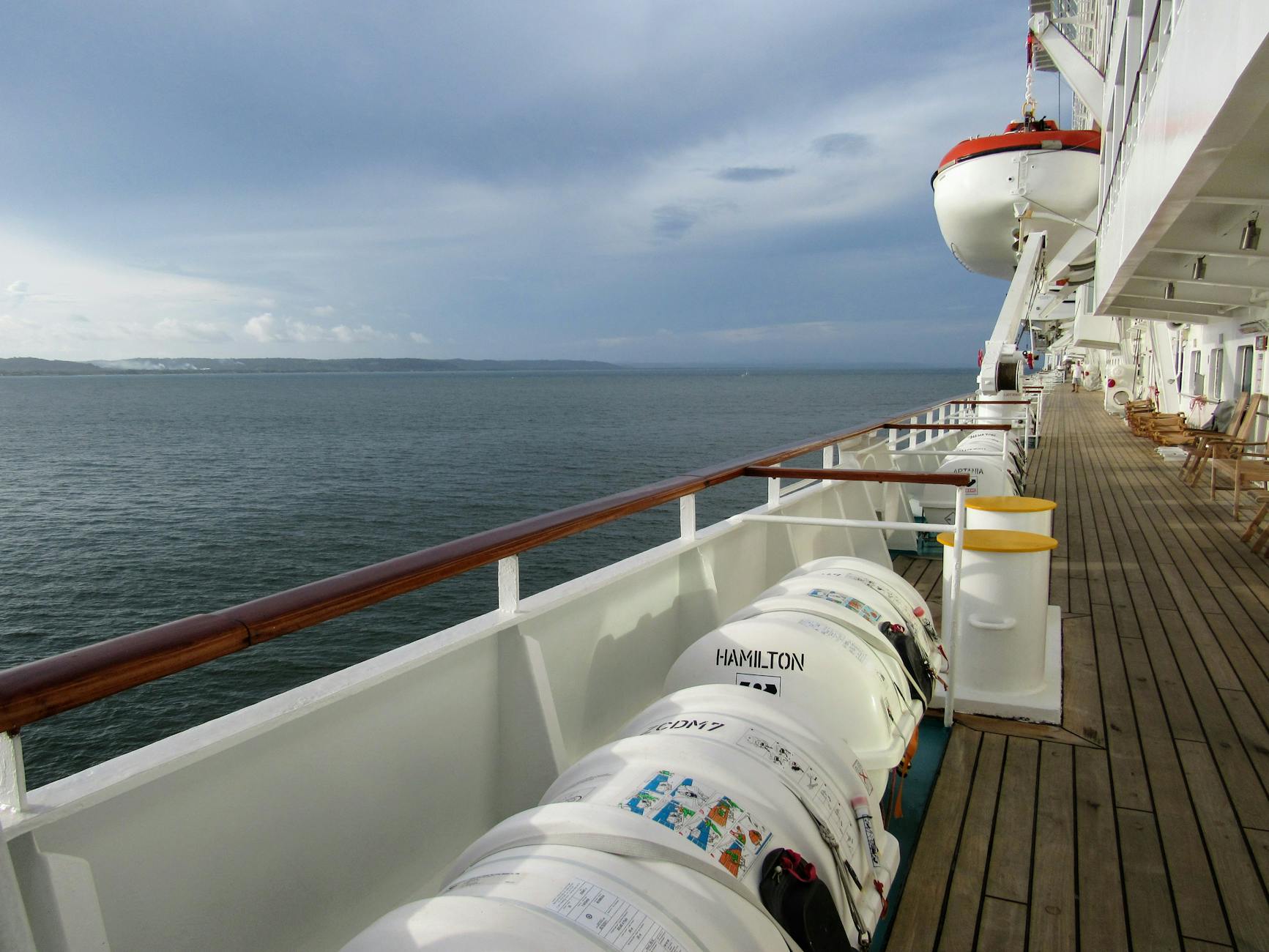 Cruise ship deck with lifeboats overlooking a calm ocean horizon