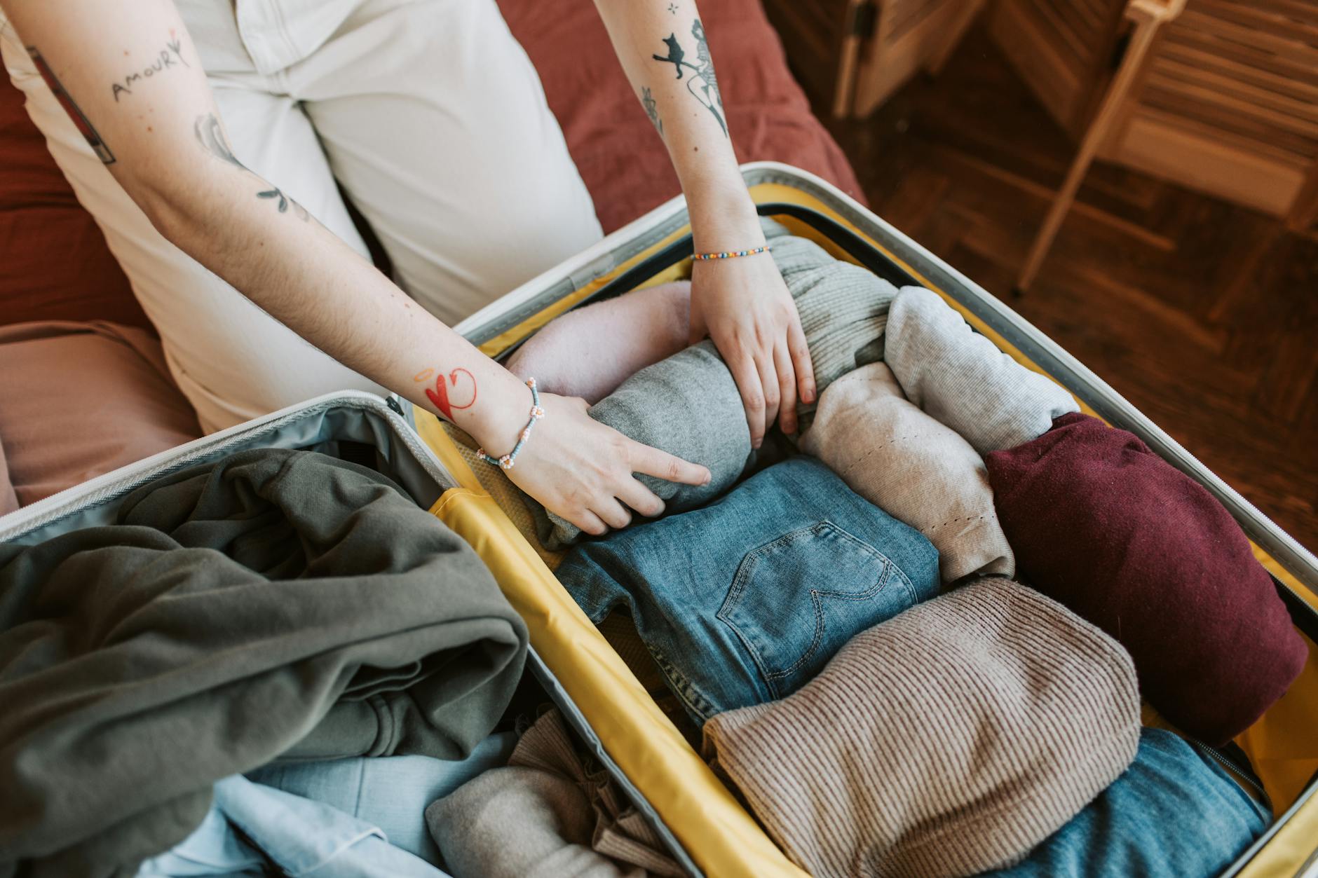 Person packing clothing items neatly into a suitcase for travel
