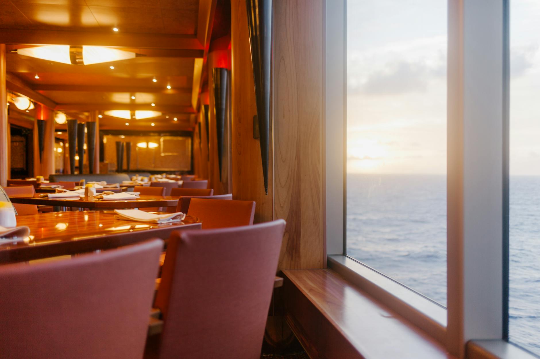Elegant dining tables on luxury cruise ship deck overlooking ocean at sunset