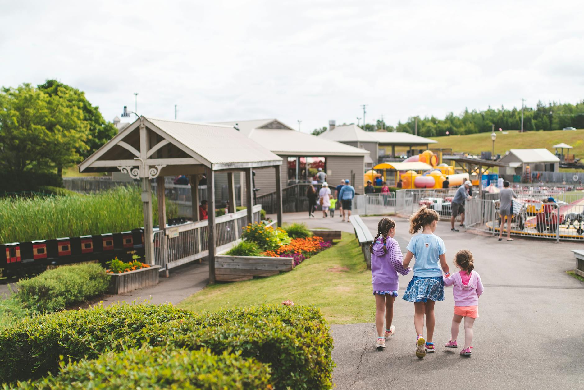 Three children walking together at an amusement park on a sunny day &mdash; the family-on-the-ground experience the budget math protects for