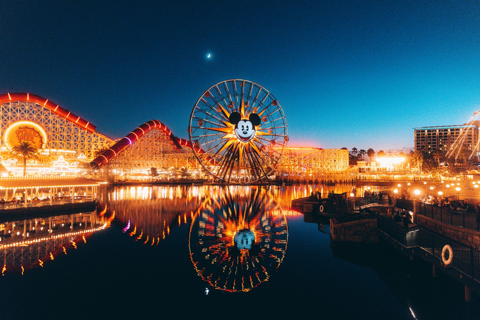 Pixar Pier at Disney California Adventure at night, the Mickey wheel and coaster lights reflected in the lagoon