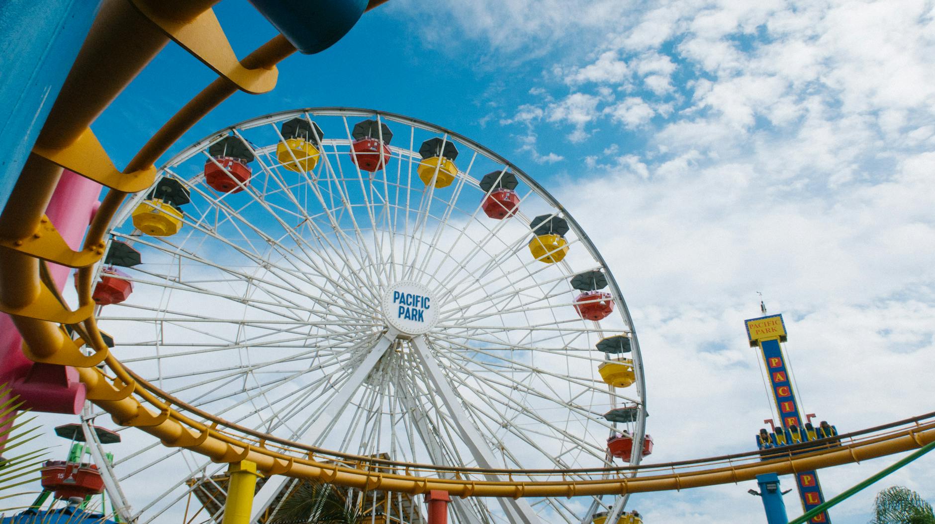 Colorful ferris wheel and roller coaster at amusement park with blue sky backdrop