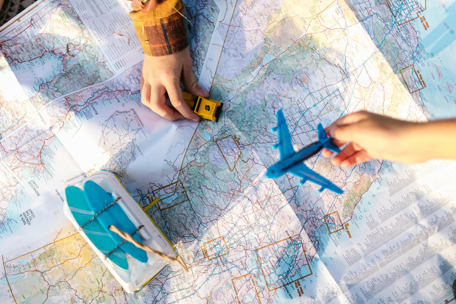 Hands holding a toy airplane and a toy car over a folded paper map, used for trip planning