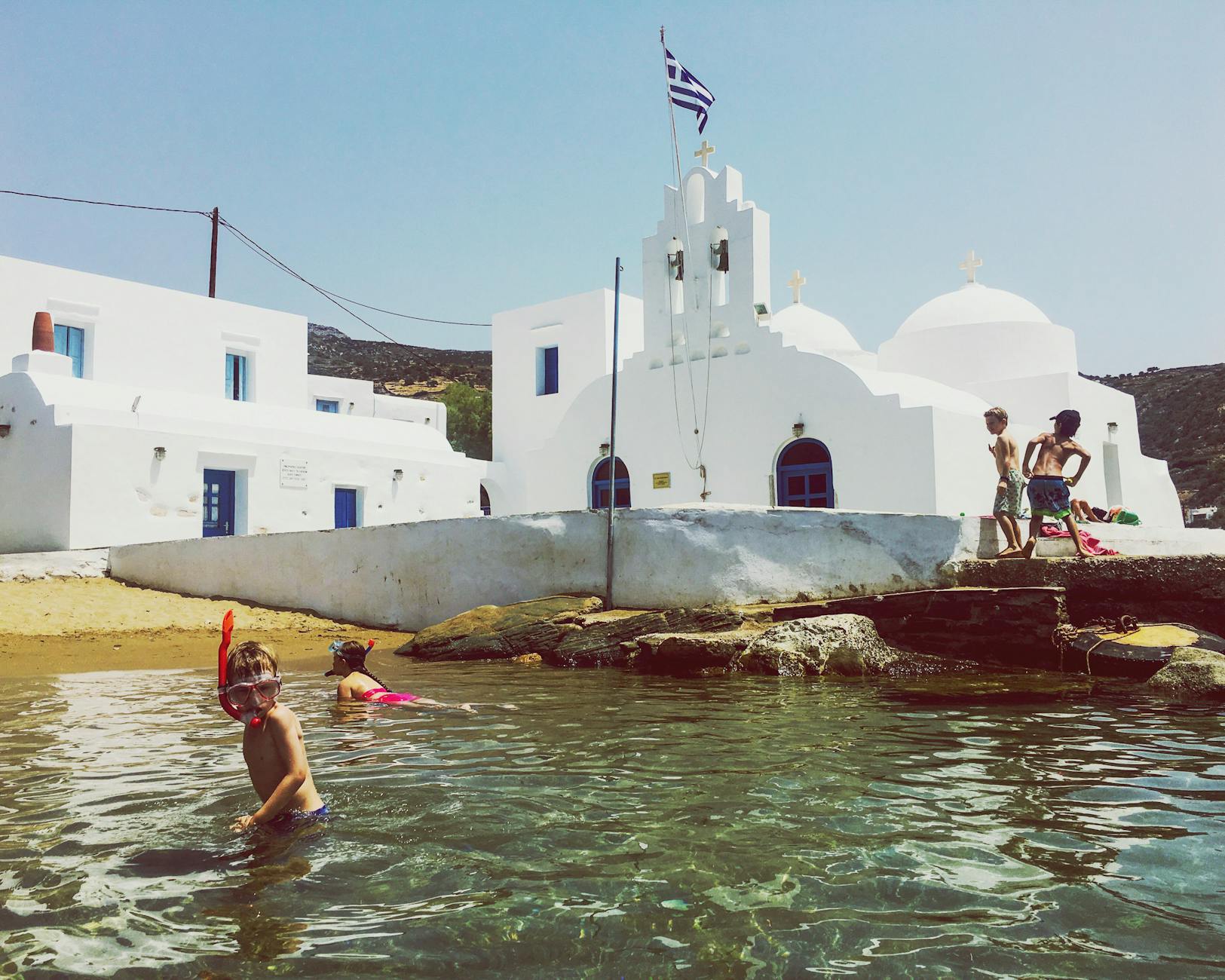 Children snorkelling near a whitewashed Greek island church on a family holiday in Greece