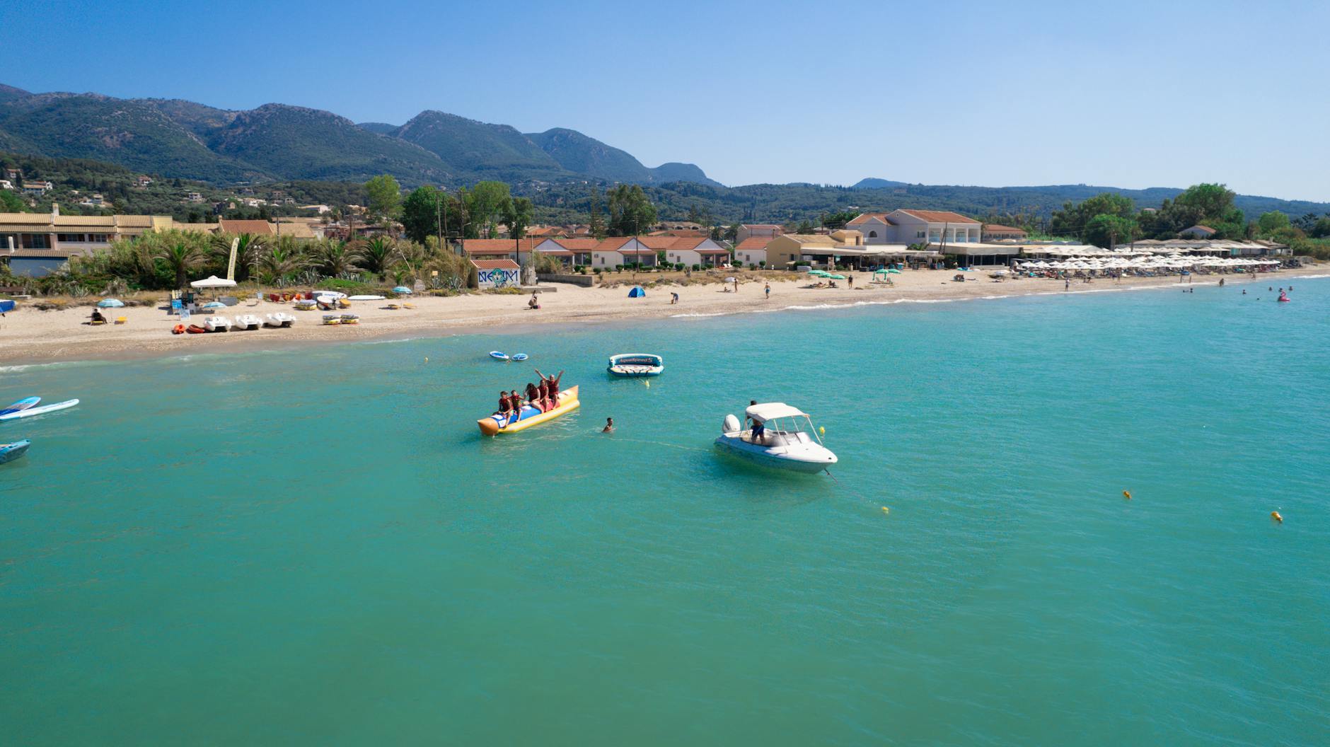 Turquoise sea at a Corfu family beach, ships anchored close to shore, typical of Greek island family holidays