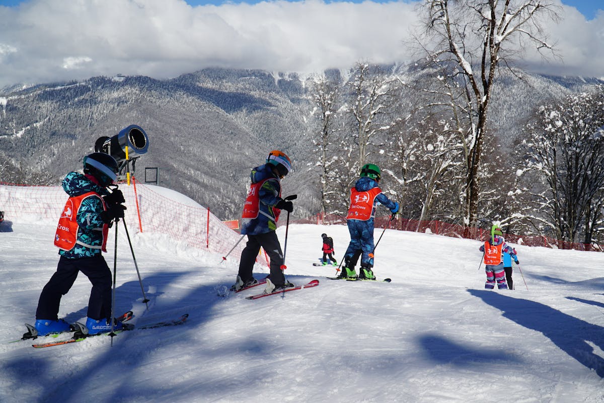 Children in colourful ski outfits learning on a snowy beginner slope during a ski school lesson
