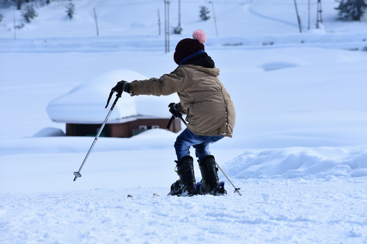 Young child on skis holding poles on flat open snow beside a snow-buried building