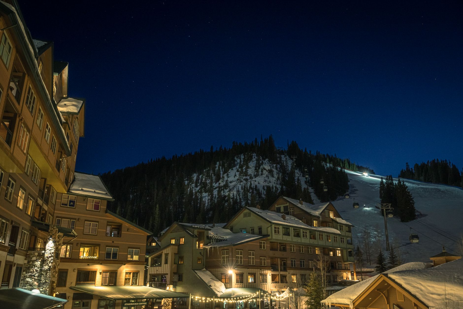 Illuminated ski resort town at night below a snow-covered mountain slope