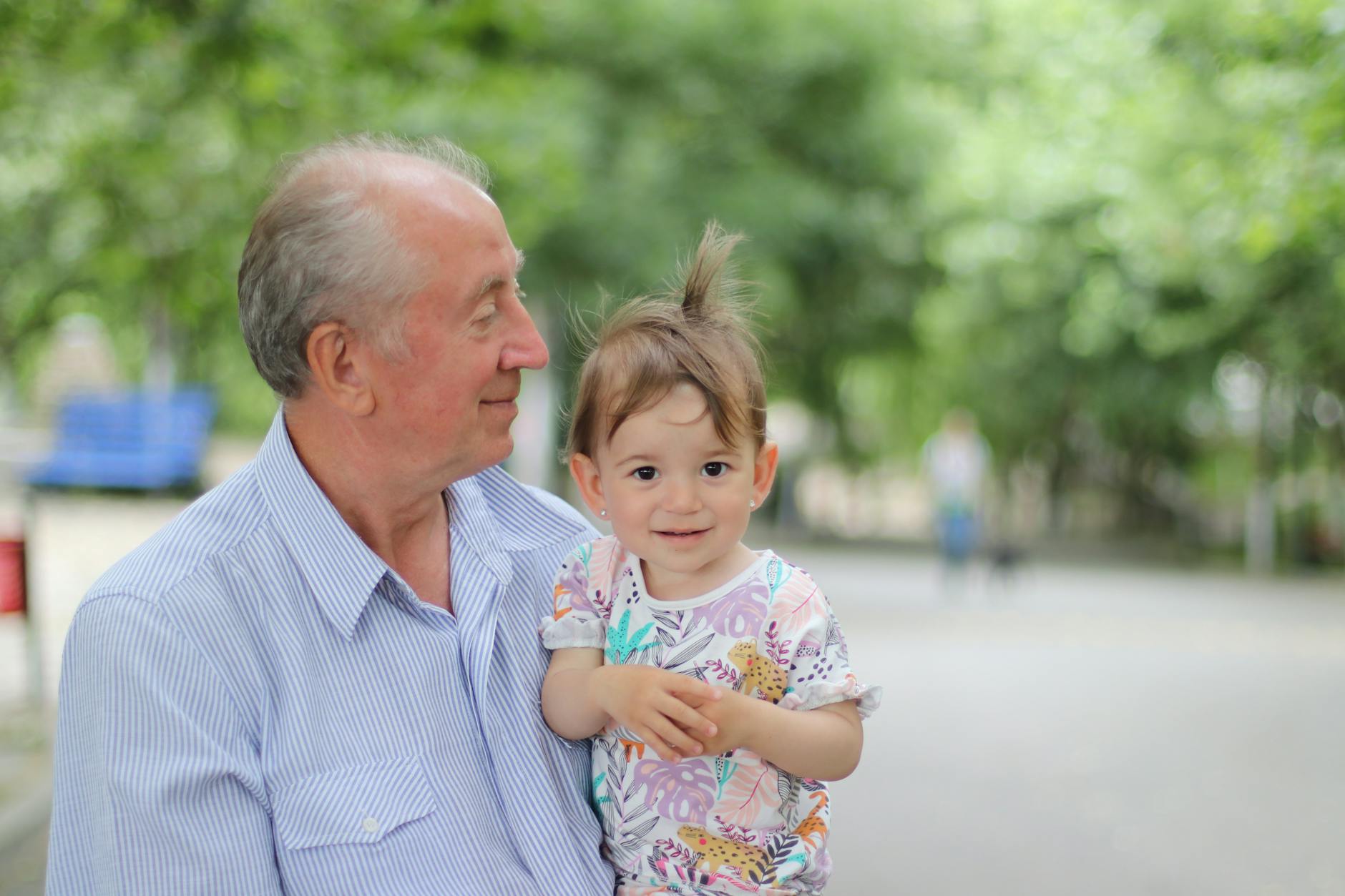 Grandfather holding his grandchild in a sunny park &mdash; the intimate skip-gen bond moment that anchors why these trips matter