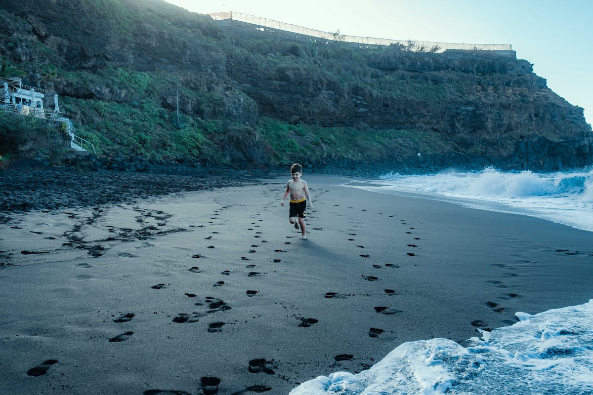 A boy runs along a black sand beach in Tenerife, the February warmth the half-term sun rows are priced against
