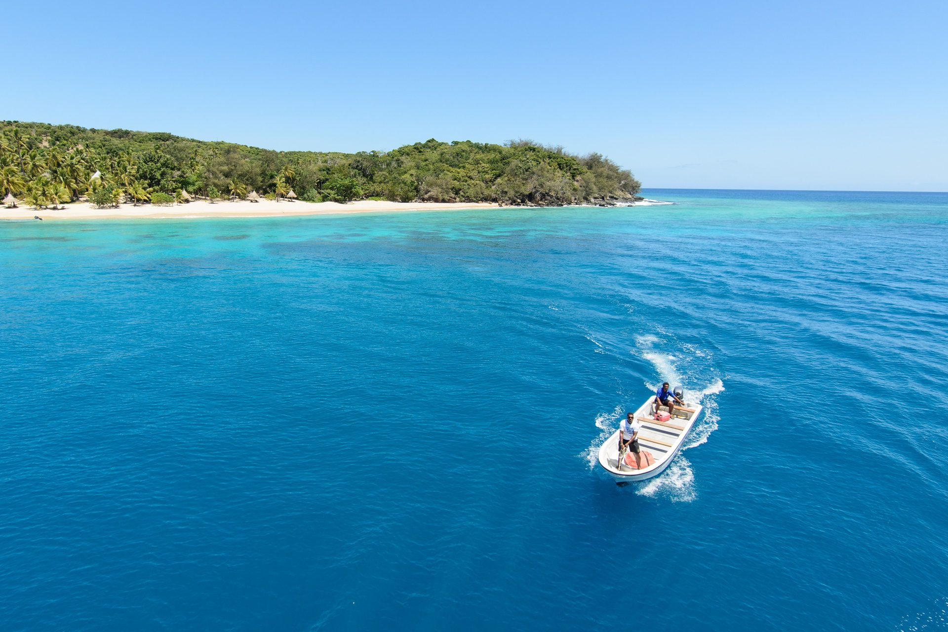 Aerial view of a motorboat crossing blue water past a tropical island, the kind of boat transfer a Mamanuca stay adds
