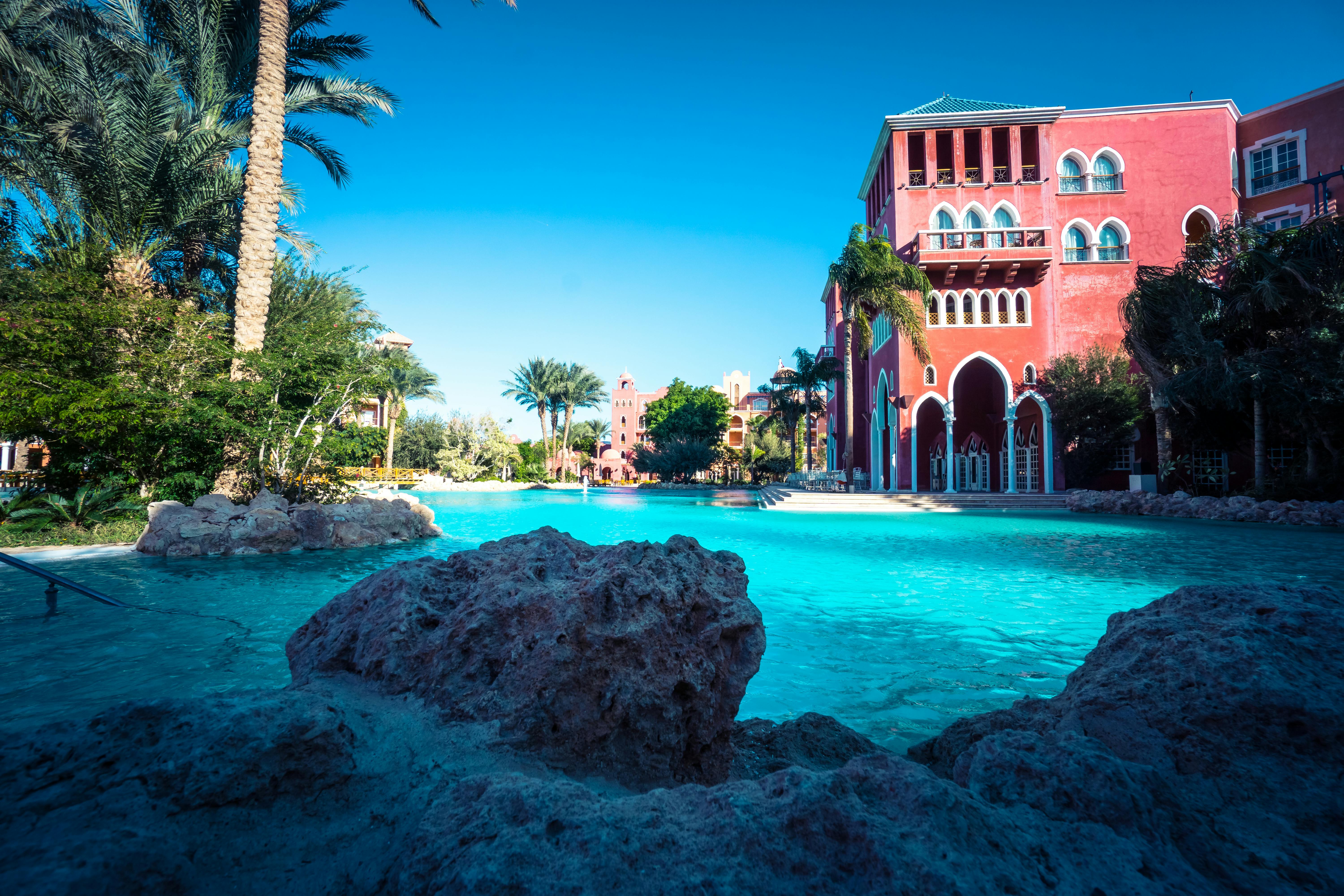 Tropical resort poolside area with palm trees and red architecture under sunny sky representing the hotel resort fees category