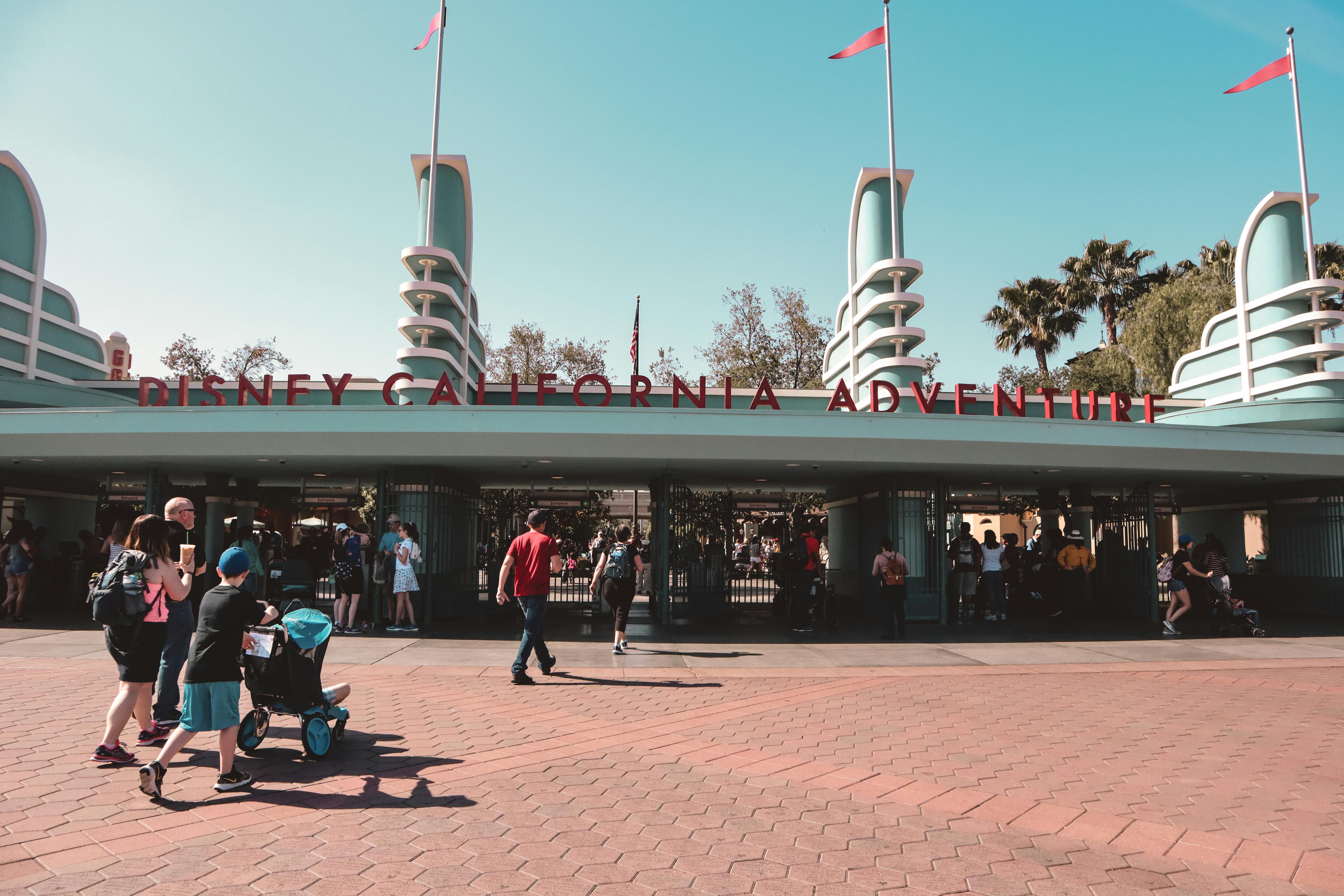 Visitors at theme park entrance gathered in front of attractions representing the parking food and souvenir hidden cost categories