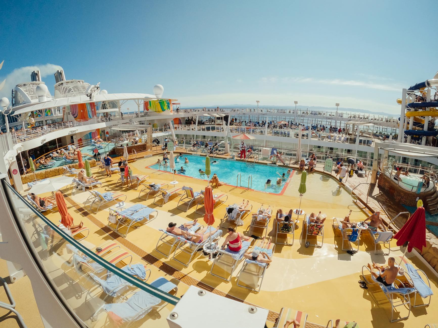 Passengers enjoying the pool area on a cruise ship deck with lounge chairs and ocean views