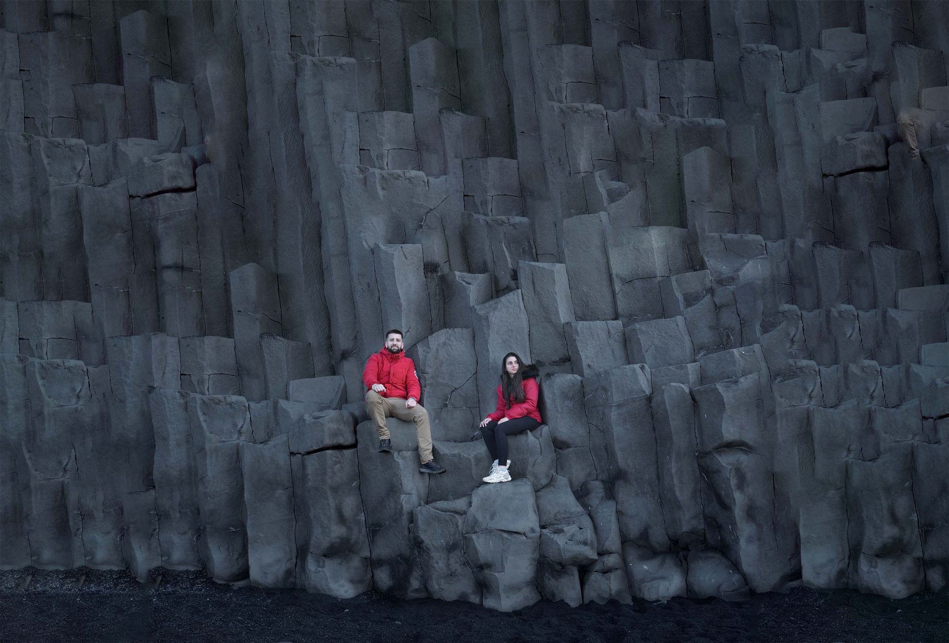 Two visitors sitting well back from the water on the basalt columns at Reynisfjara black sand beach, south Iceland