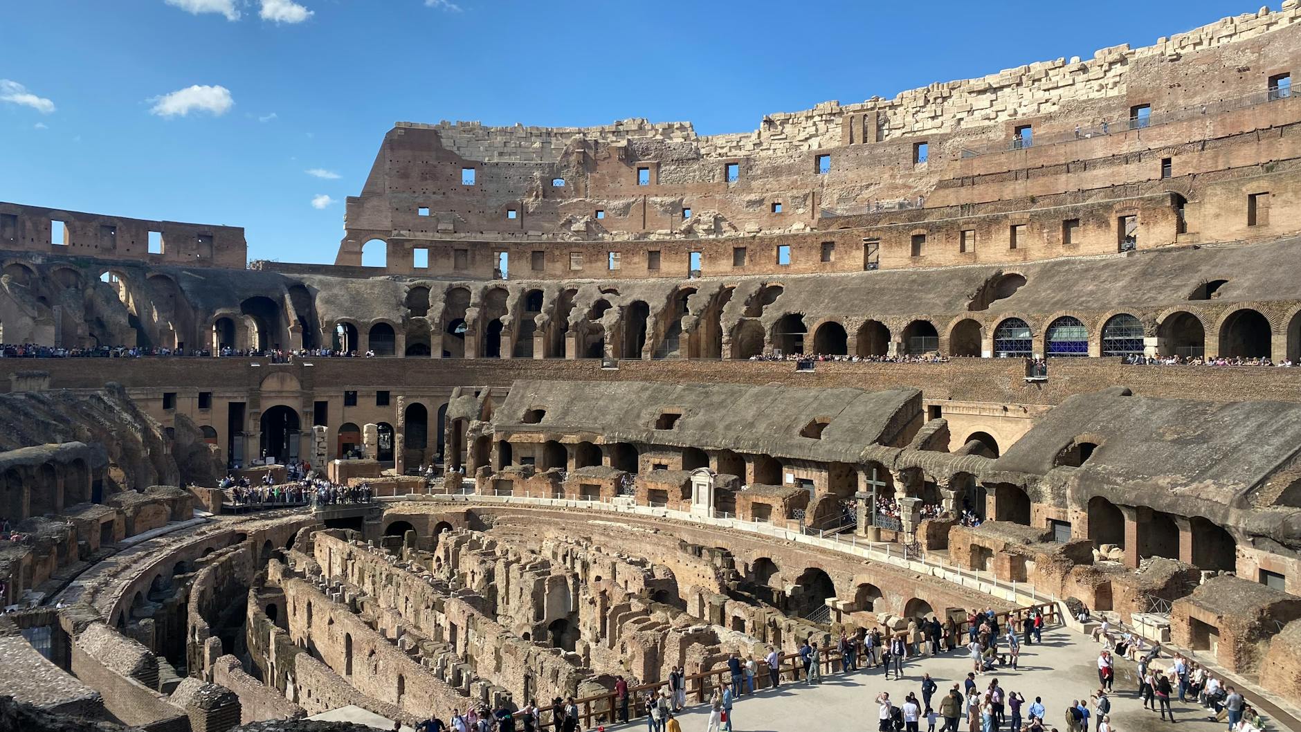 Tourists exploring the interior of the ancient Roman Colosseum under sunny skies