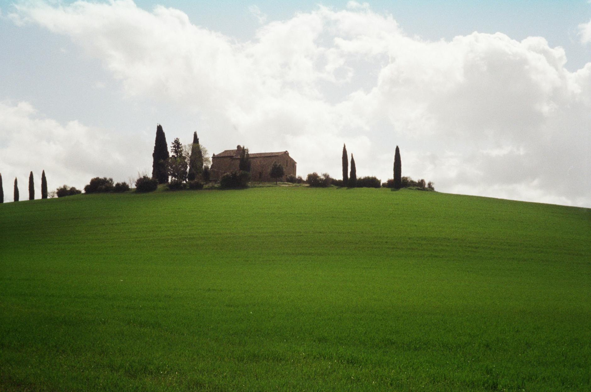 A serene Tuscan landscape with a farmhouse atop a green hill dotted with cypress trees &mdash; the agriturismo countryside that defines a slower-paced Italian family vacation