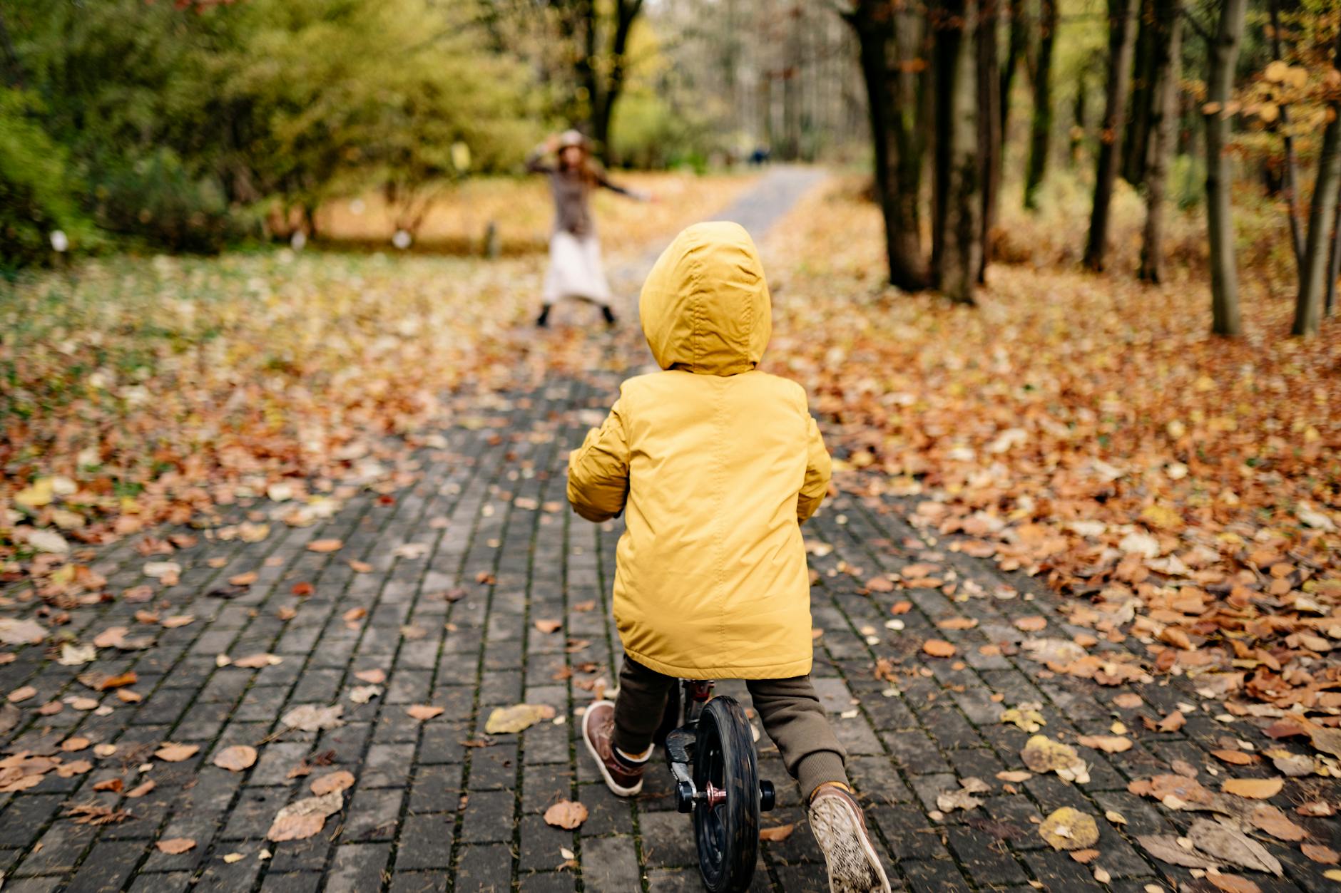 Child in yellow jacket riding a bicycle through an autumn park path