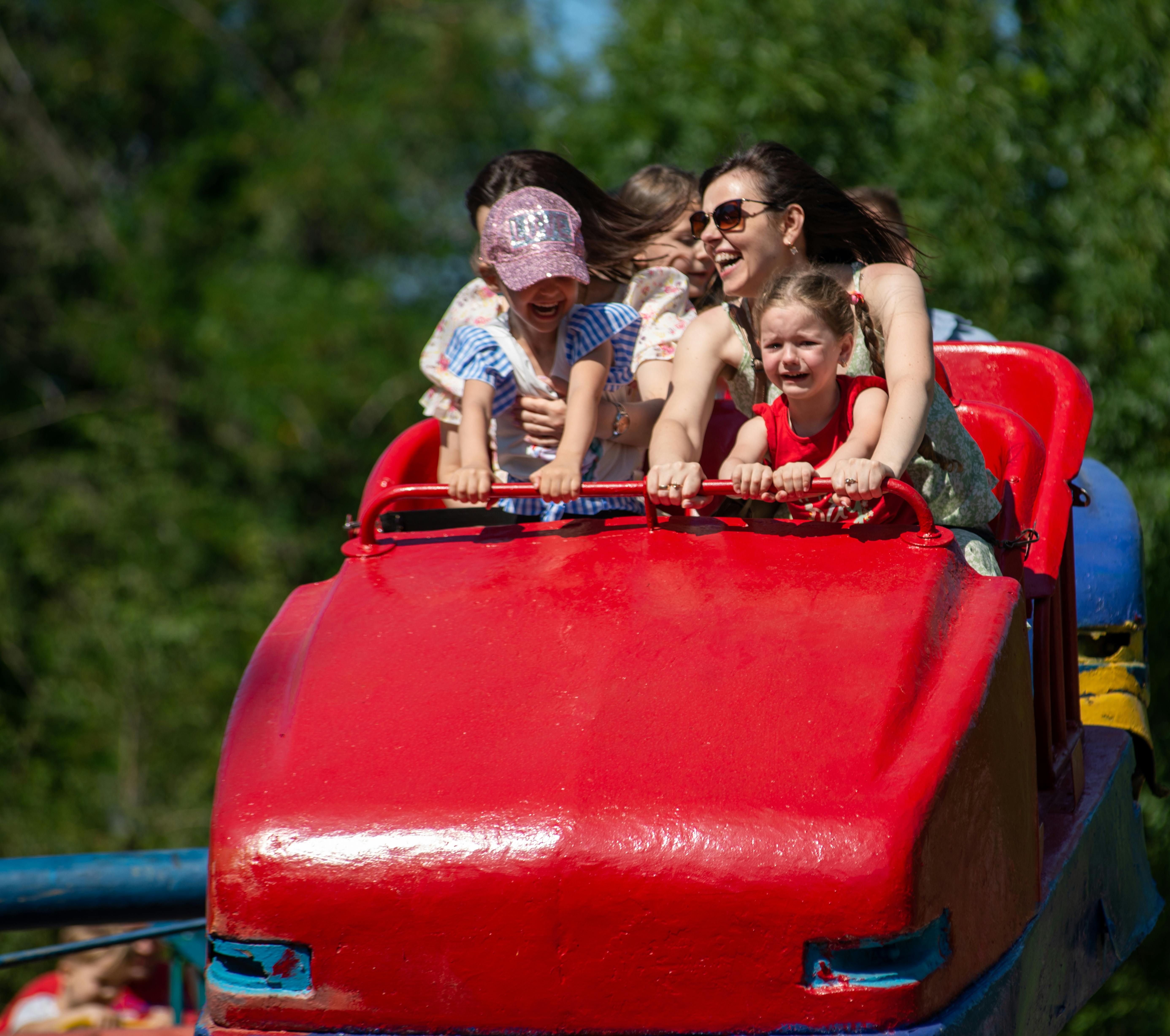 Family with children riding a red roller coaster mid-loop showing the joy that anchors the Orlando theme park experience