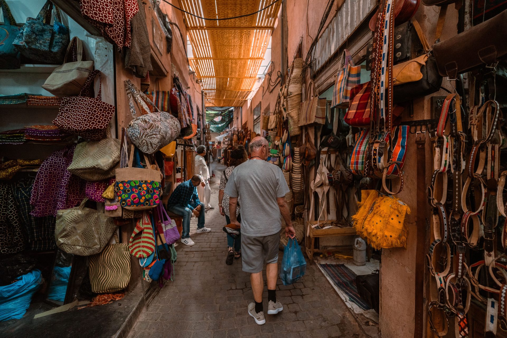 A narrow covered souk alley in Marrakech hung with bags and leather goods, with shoppers walking single file