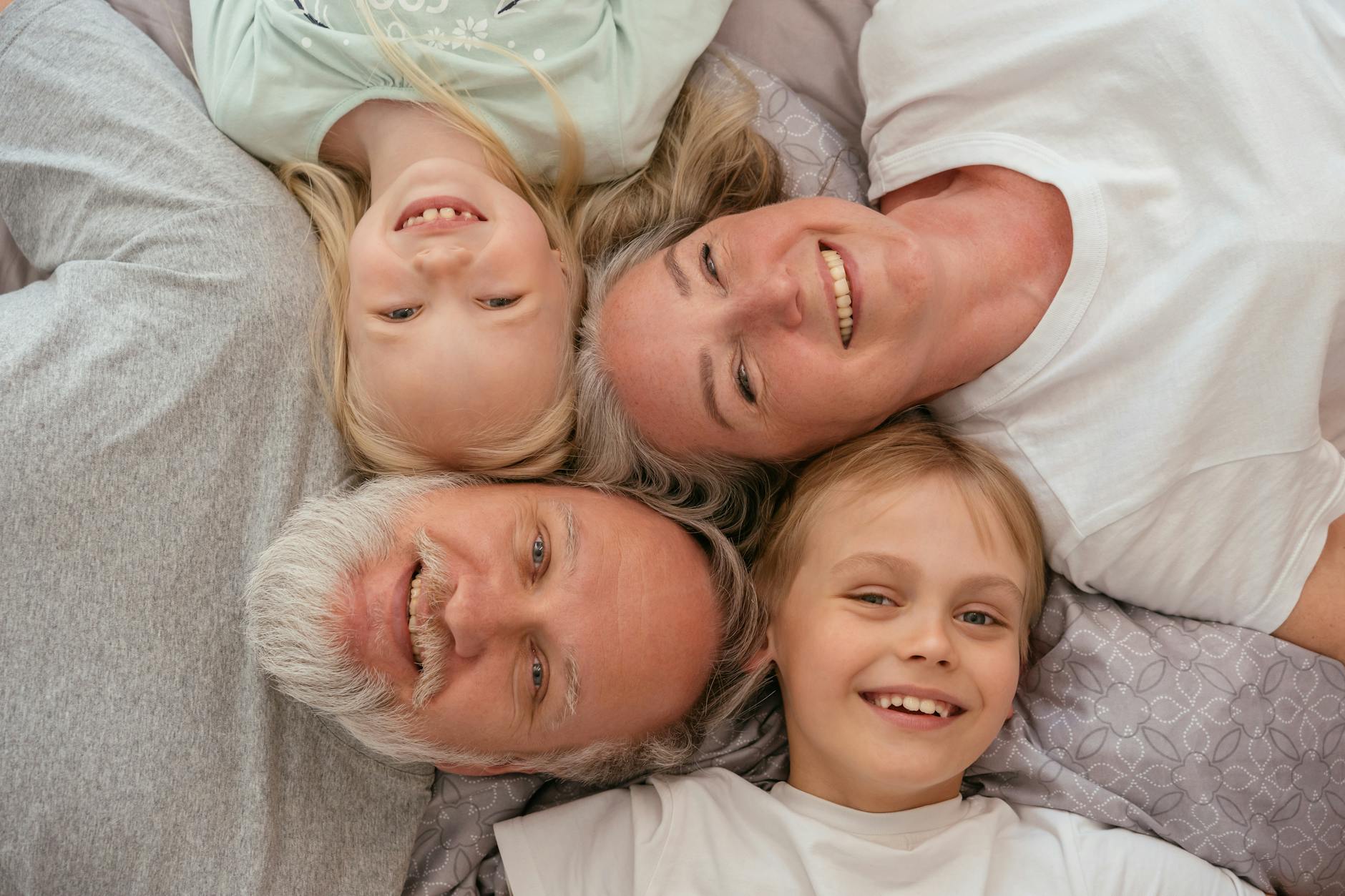 Joyful multigenerational family lying down and smiling together &mdash; the indoor lived-experience moment of a multigen vacation