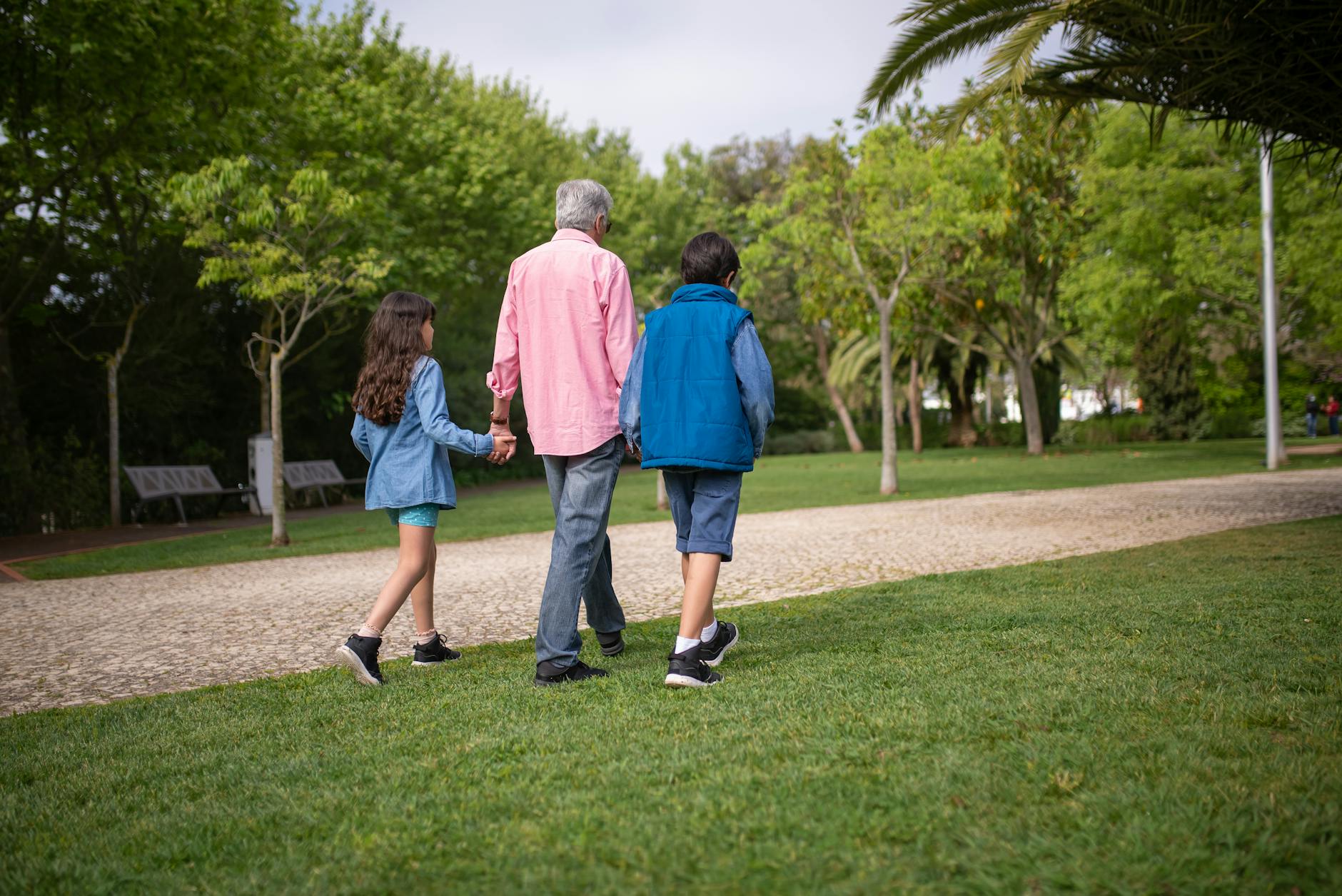 Grandfather walking with grandchildren in a lush green park &mdash; the grandparent-grandchild bond that anchors many multigenerational trips