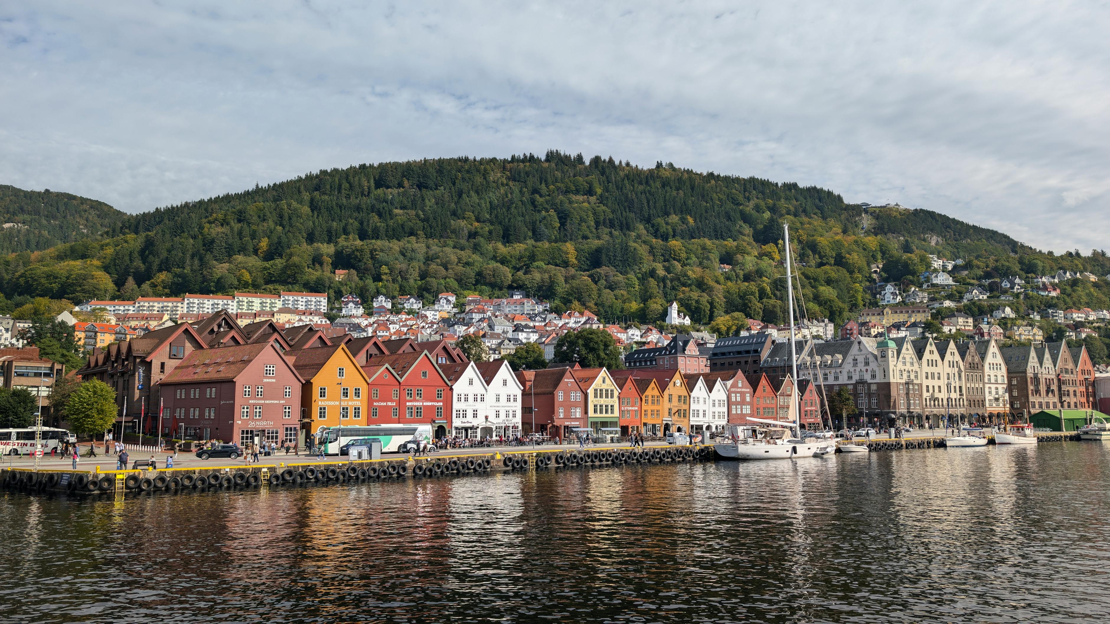 Colorful historic Bryggen Wharf in Bergen with lush hills and calm harbor water &mdash; the UNESCO-listed Hanseatic waterfront that anchors a Bergen-based fjord trip