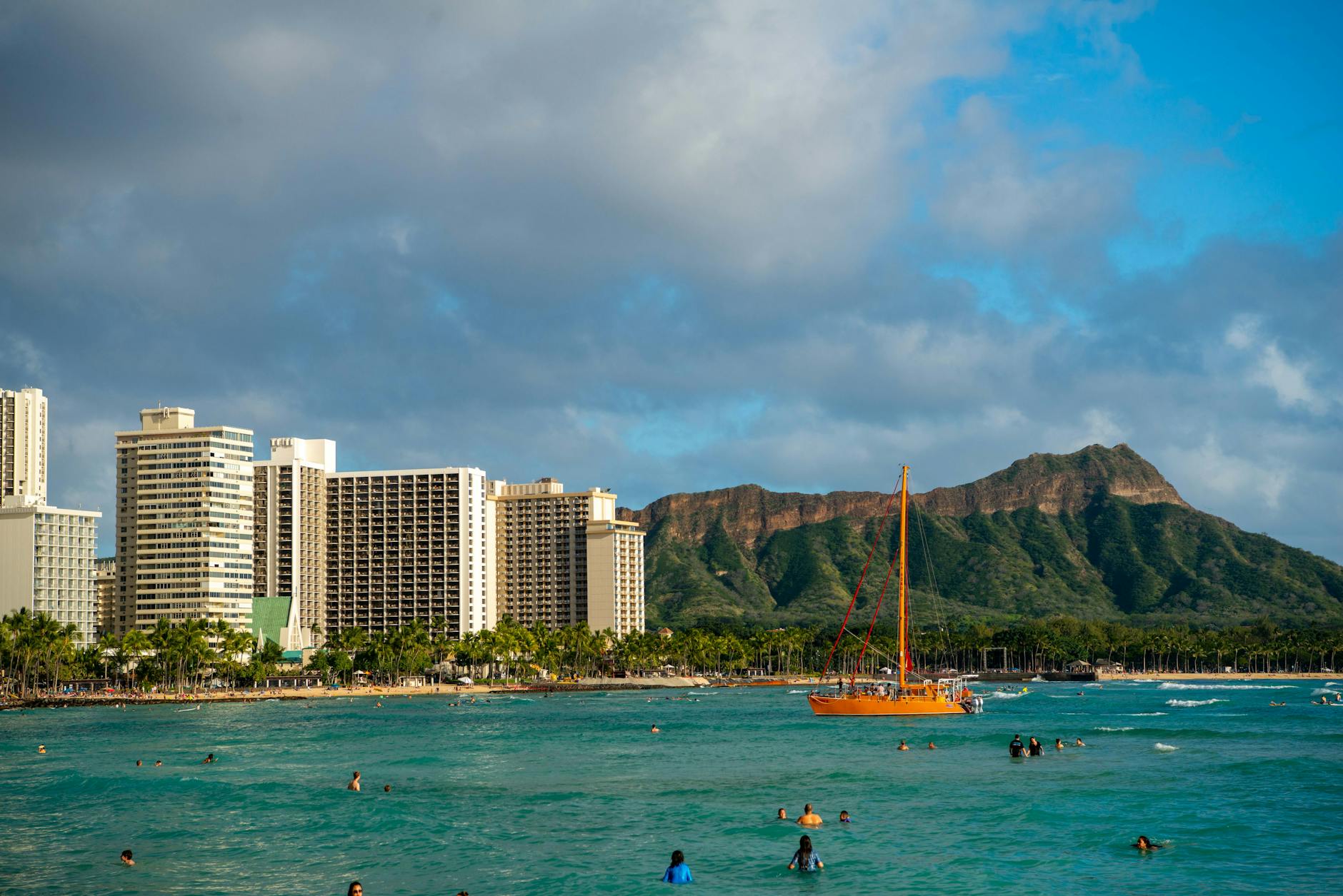 Waikiki Beach view with Diamond Head mountain and orange sailboat in the ocean