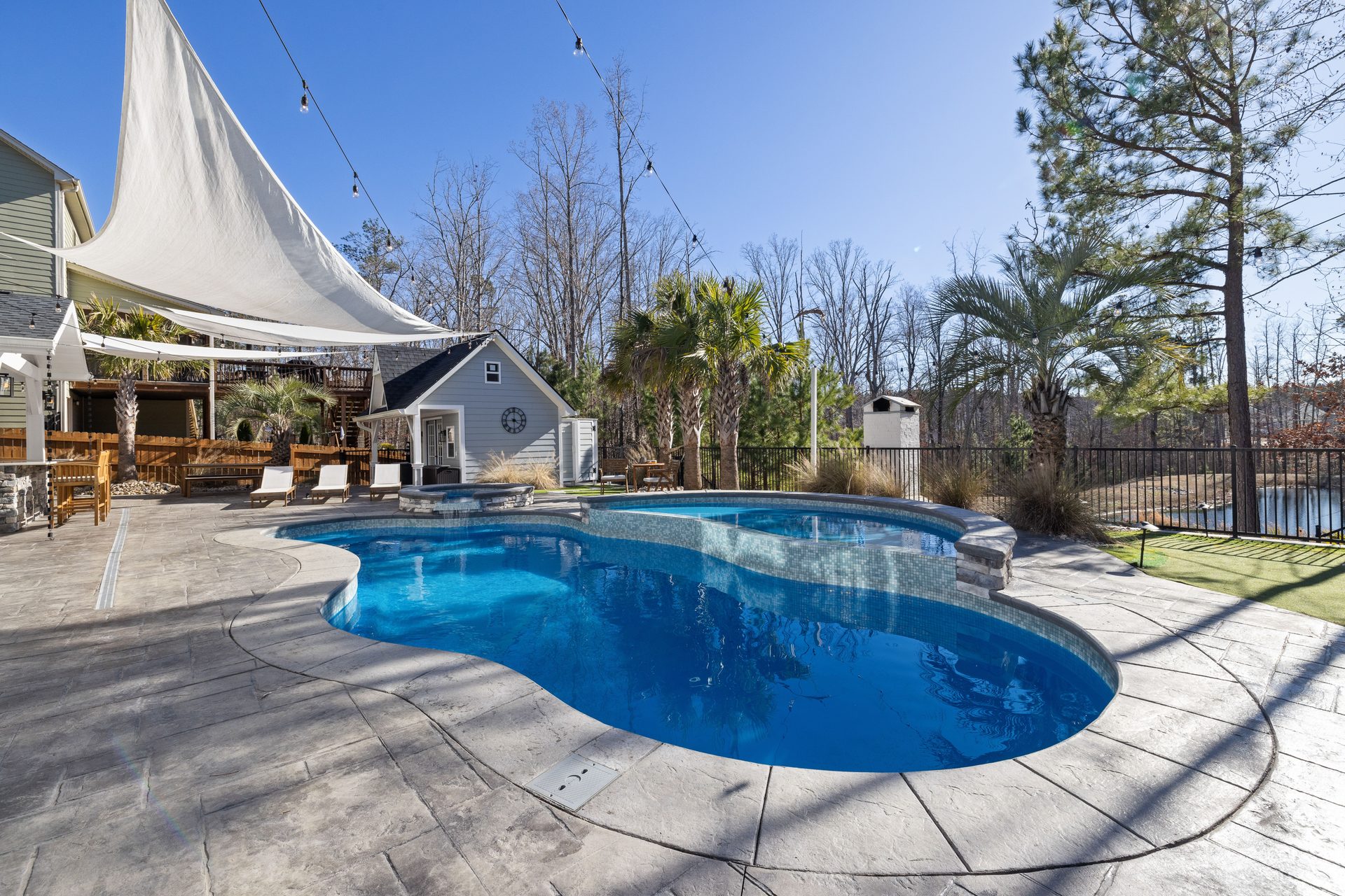 A backyard swimming pool with a wooden deck and palm trees under a blue sky, like a Kissimmee villa pool