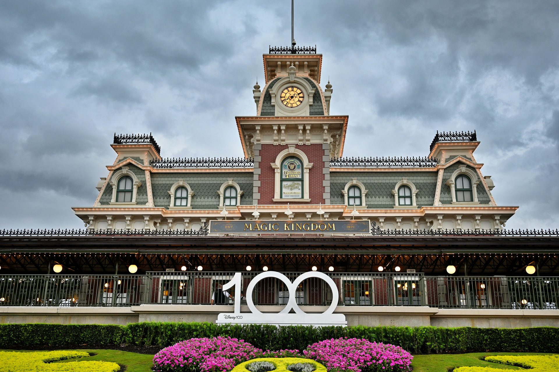 The Magic Kingdom railroad station at Walt Disney World in Orlando under a grey storm sky, with flower beds in front