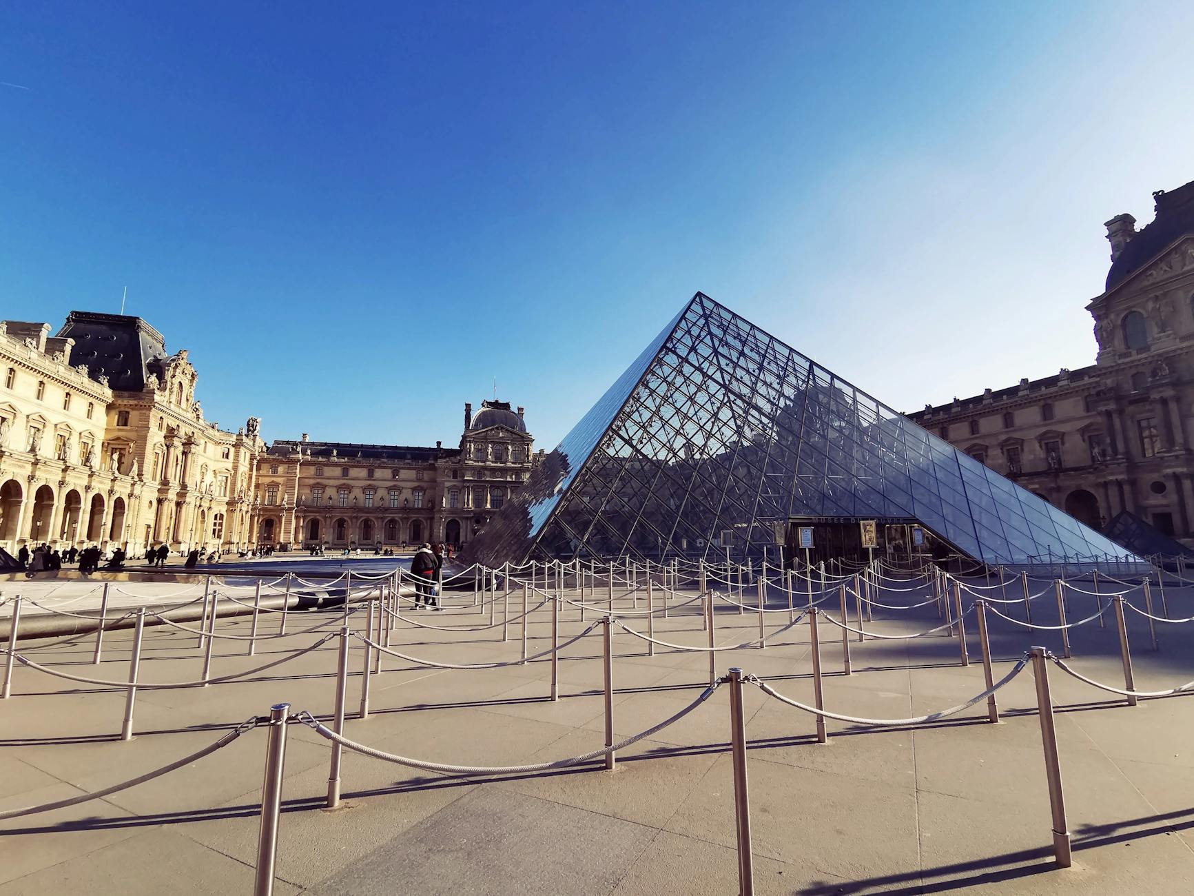 Louvre Pyramid in Paris on a bright day with clear reflections in the plaza fountains