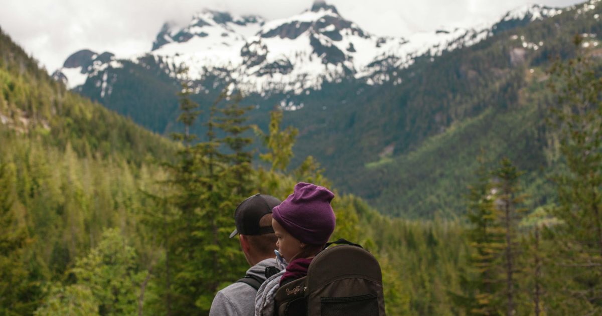 Father carrying child in hiking backpack on mountain trail