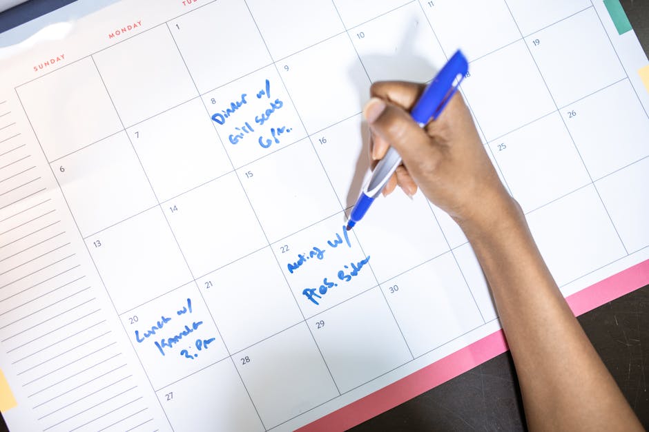 Person writing travel dates on a planning calendar with a blue pen
