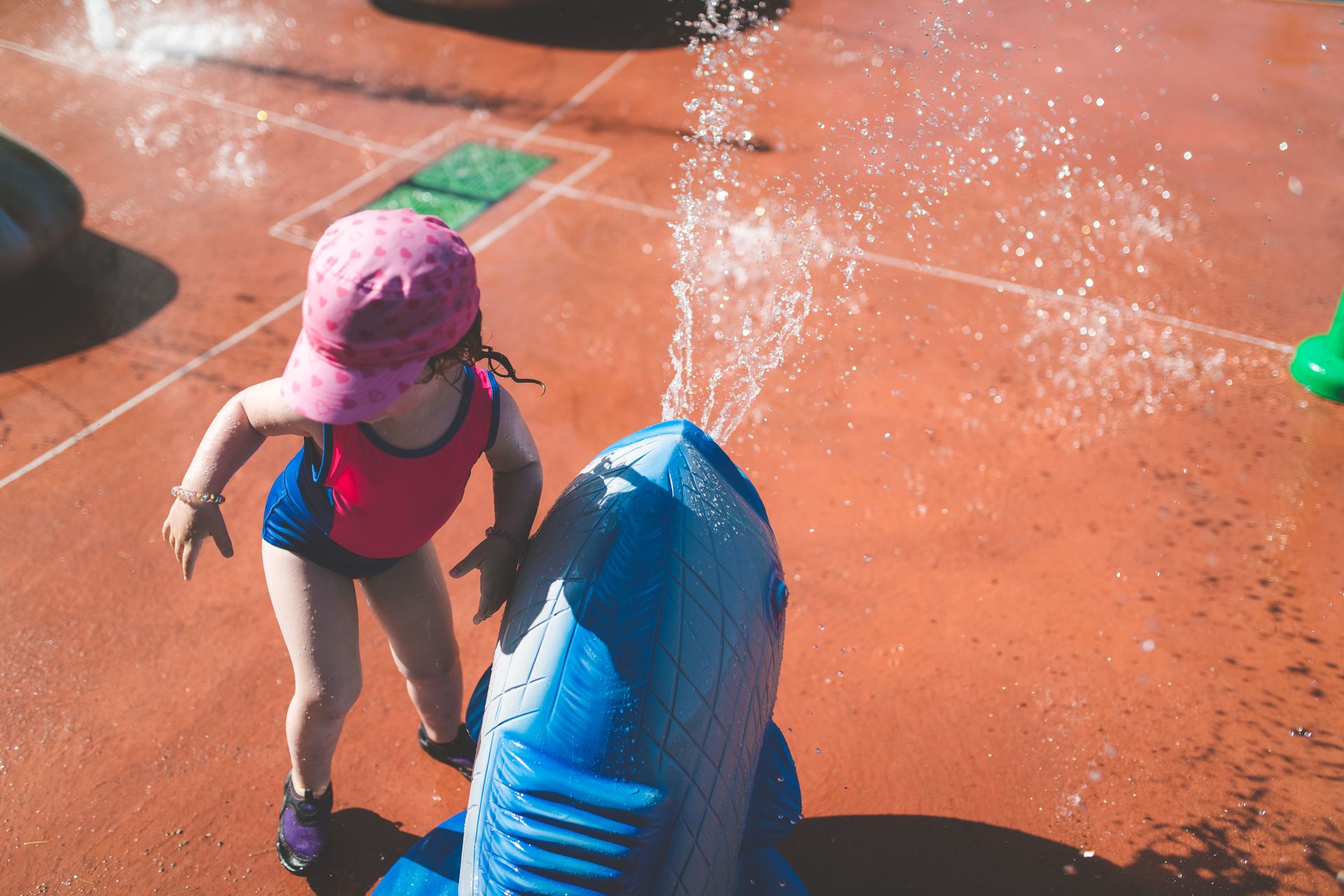 A toddler in a sun hat plays at a splash pad