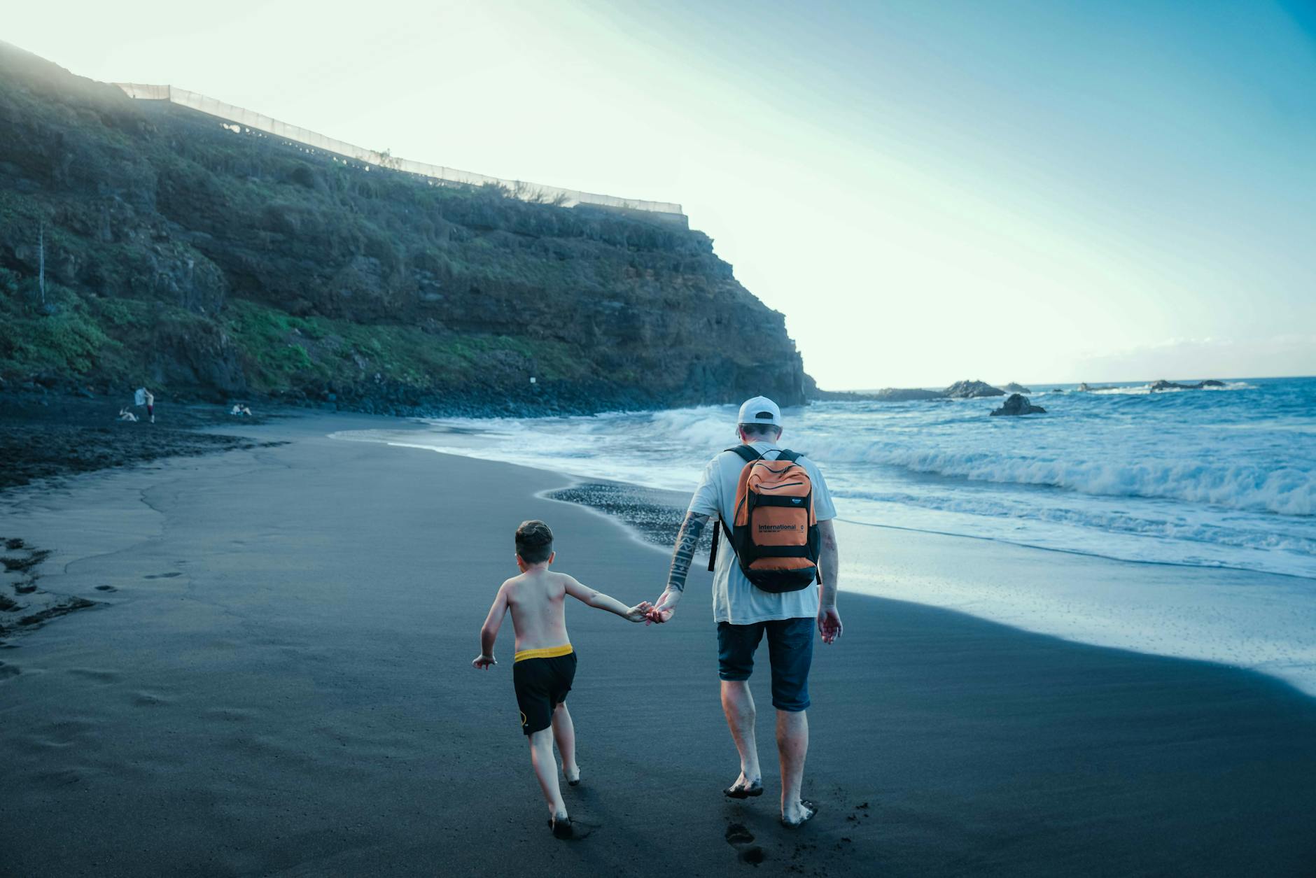 Father and young son walking on a black sand beach in Tenerife on a sunny day