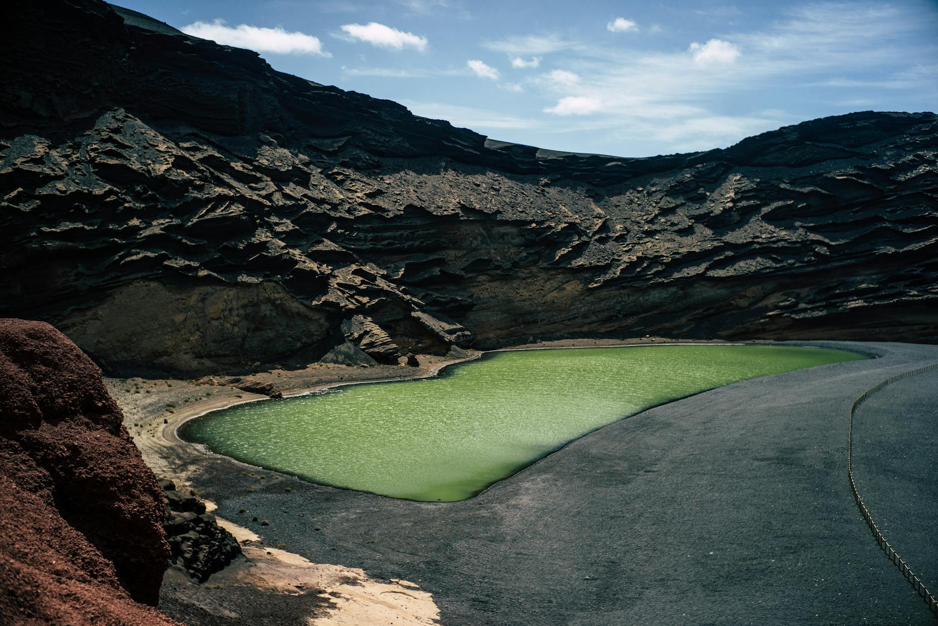 Dramatic volcanic landscape of Lanzarote with green lagoon and dark lava rocks